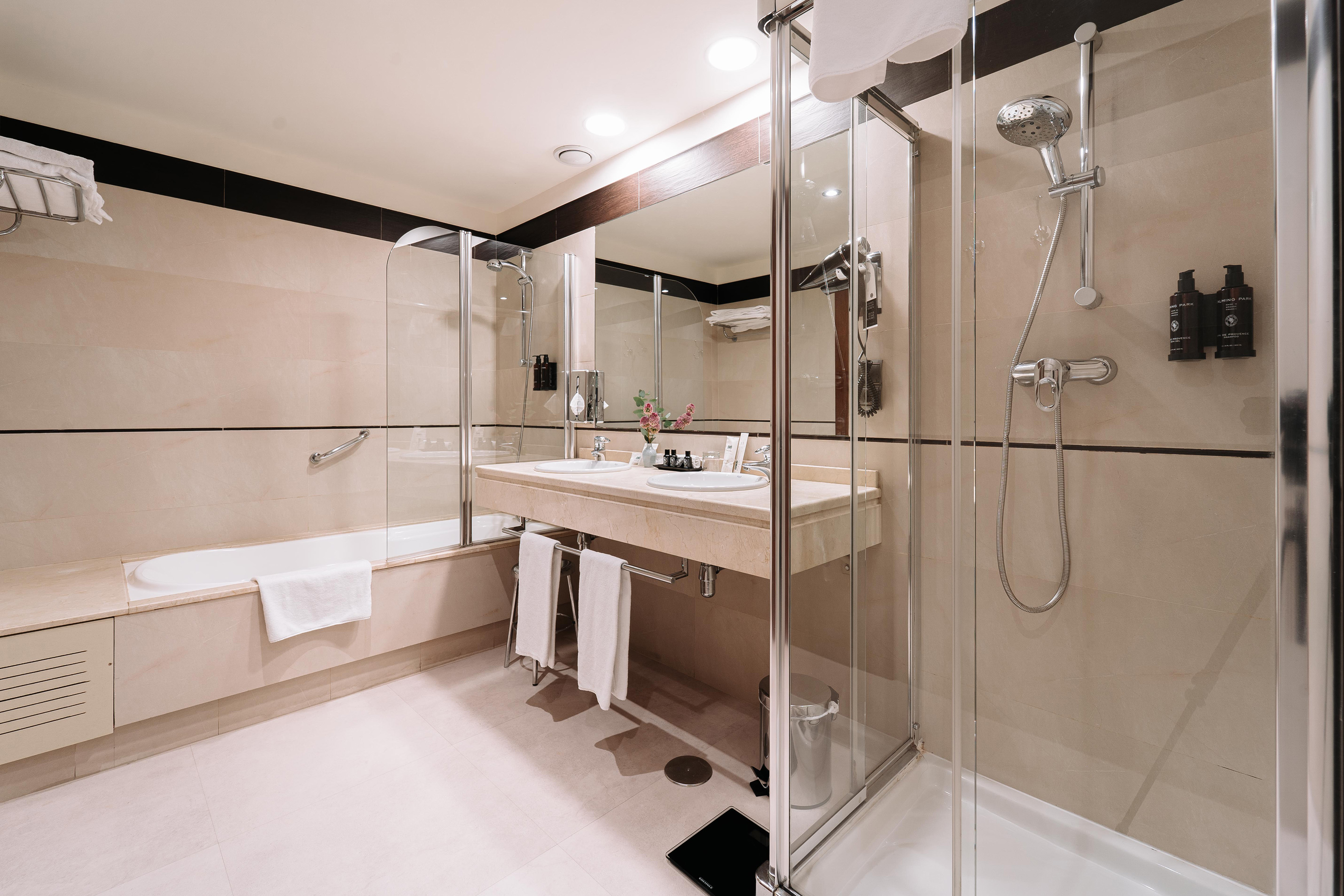 Modern hotel bathroom with double vanity, walk-in shower, and bathtub.