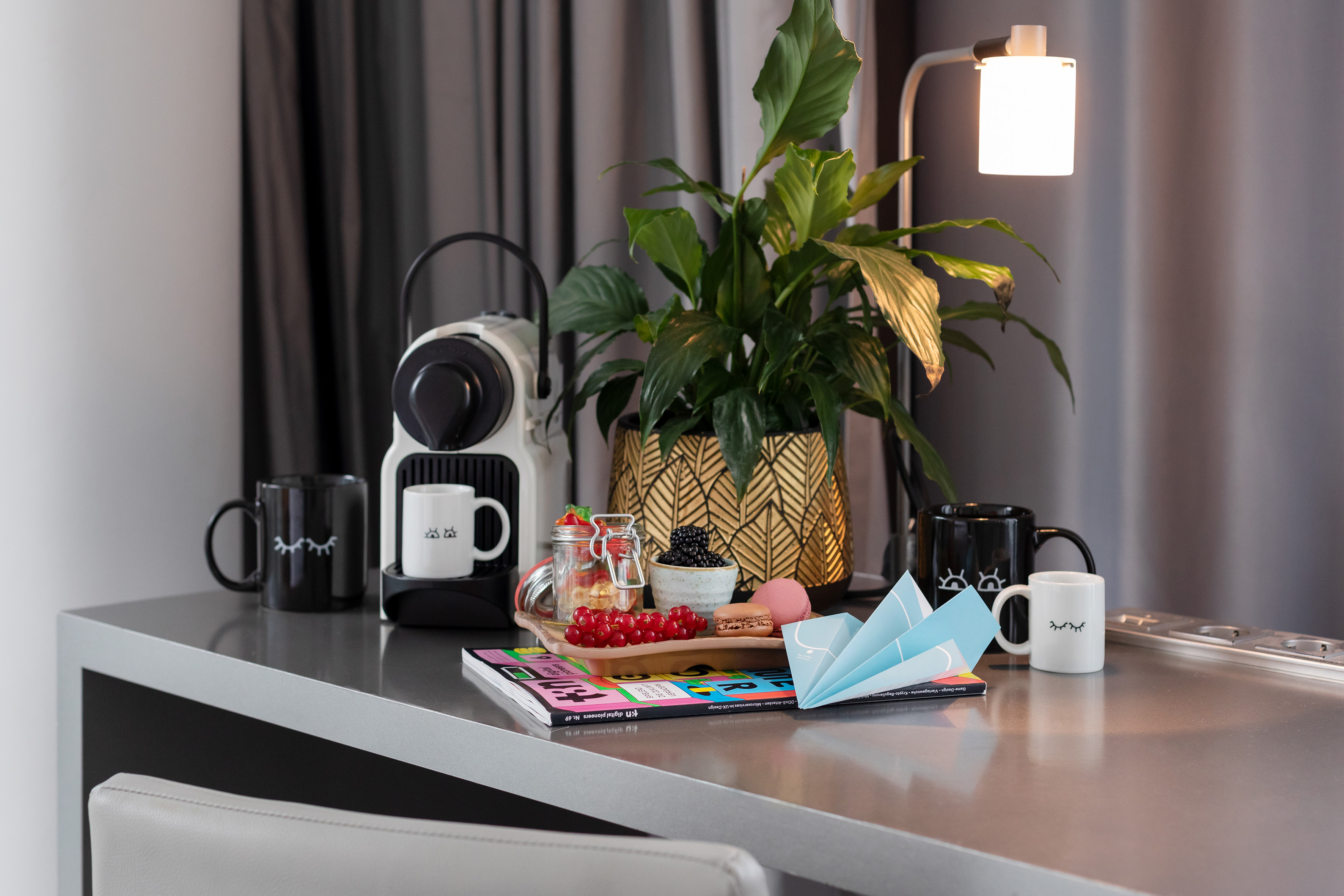 Nespresso coffee machine, plant, berries, macarons, and mugs on a modern desk.