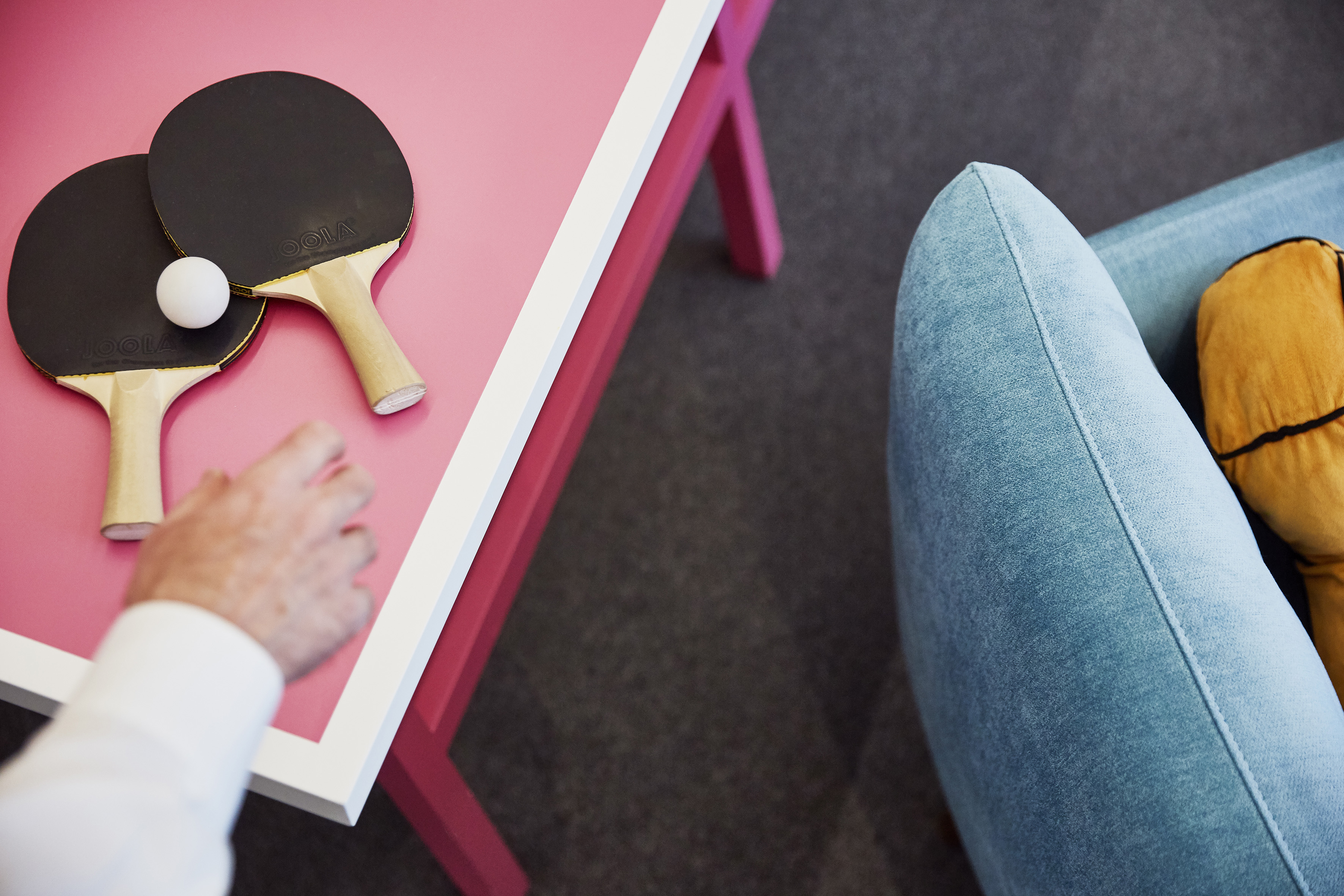 Table tennis paddles and ball on a vibrant pink table; player's hand.