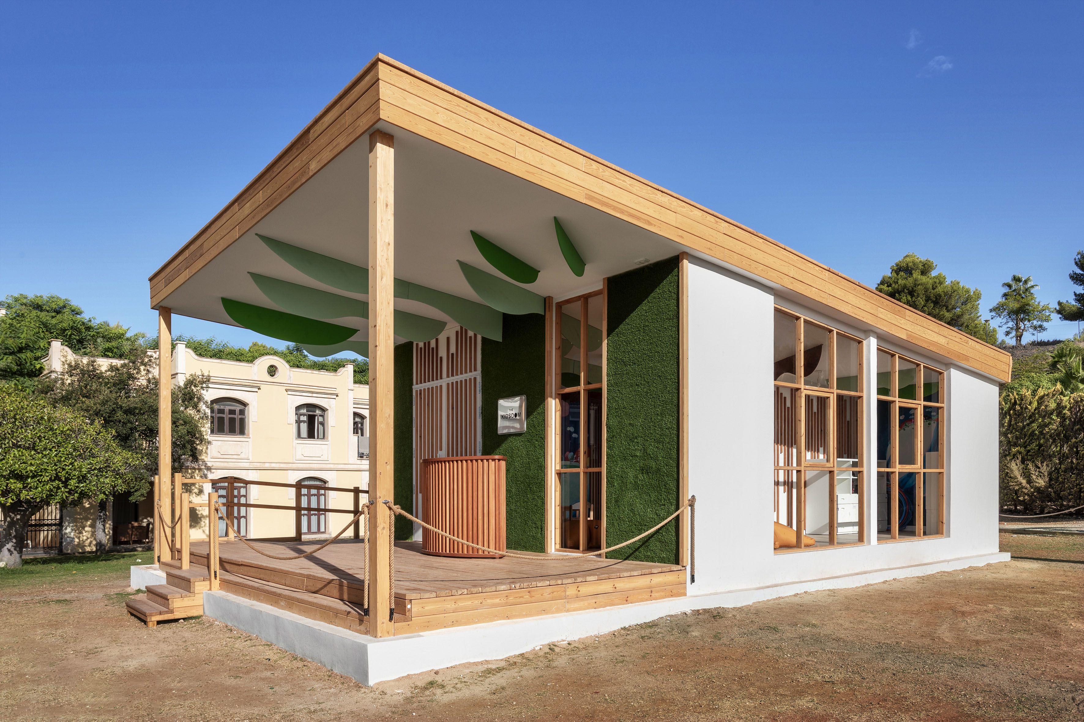 Modular wooden building with outdoor deck, green turf wall, and leaf ceiling.