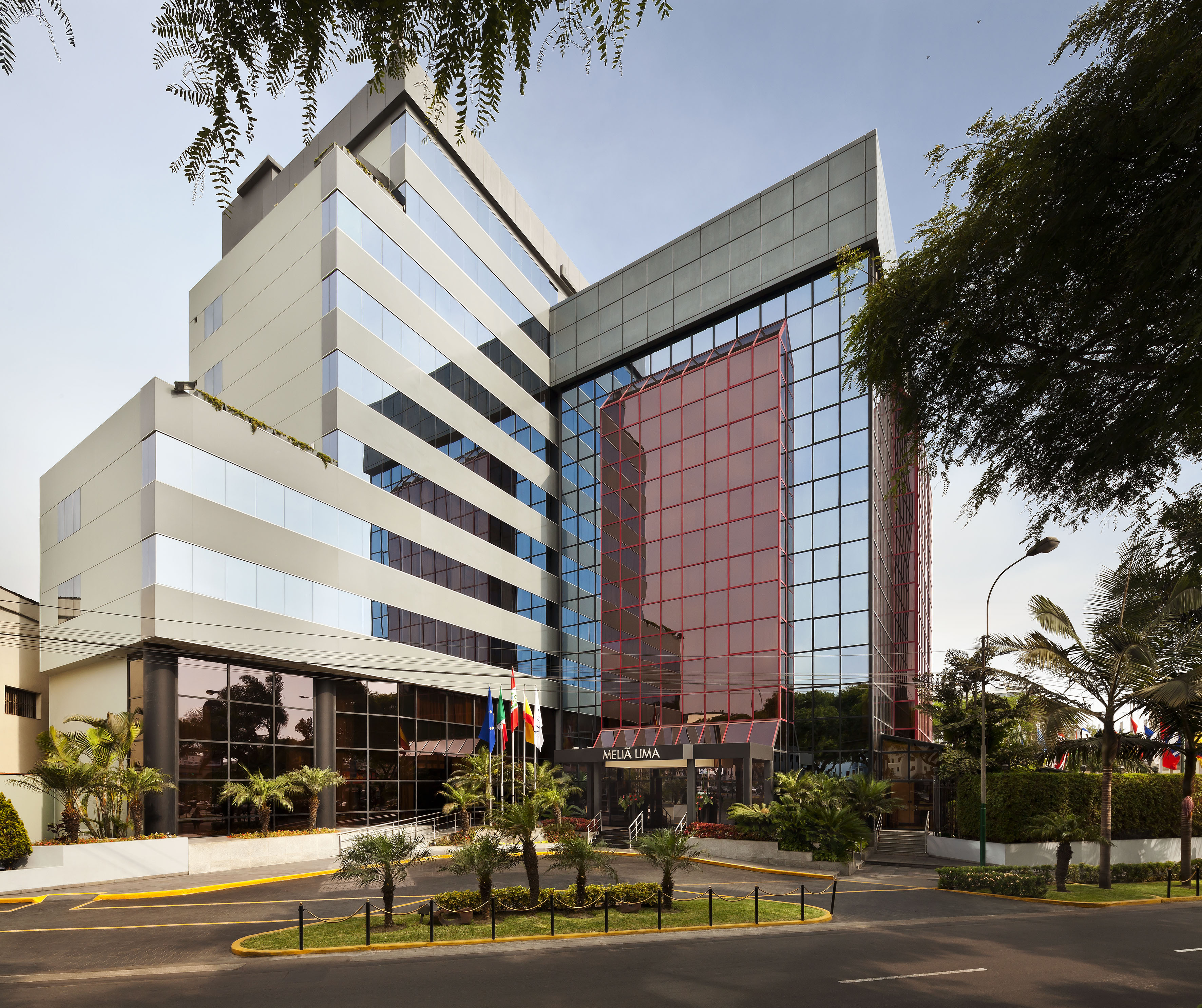 Melia Lima Hotel exterior: modern glass facade, red accents, palm trees.