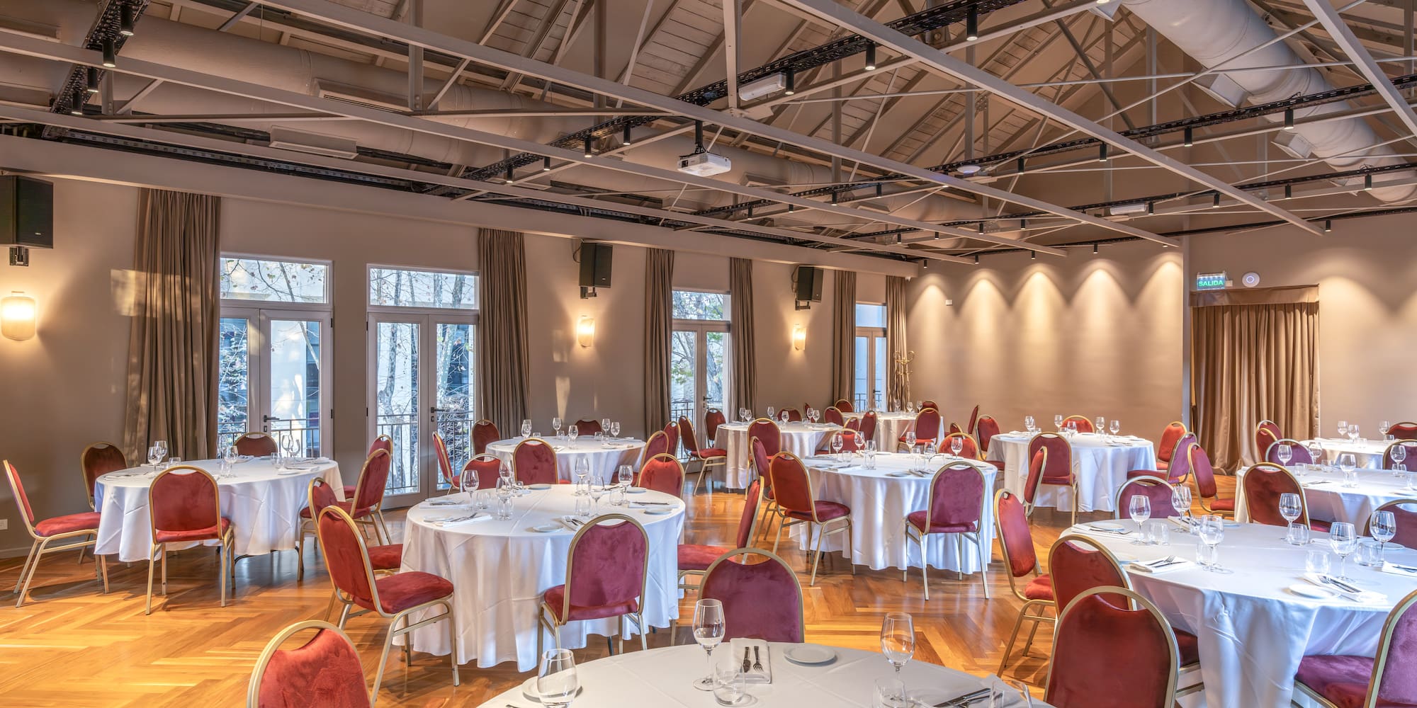 Spacious banquet hall set with round tables, red velvet chairs, and exposed beams.