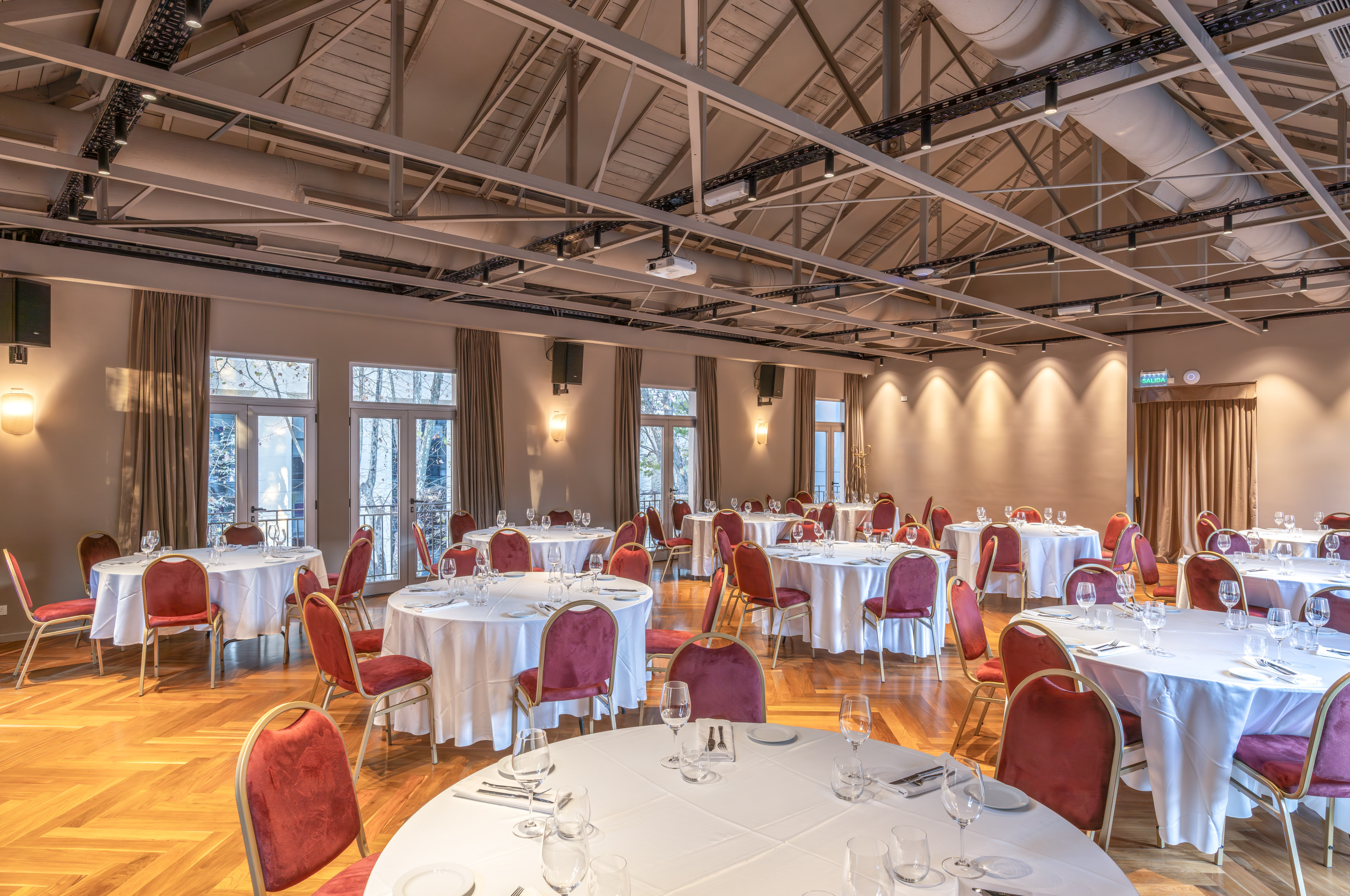 Spacious banquet hall set with round tables, red velvet chairs, and exposed beams.
