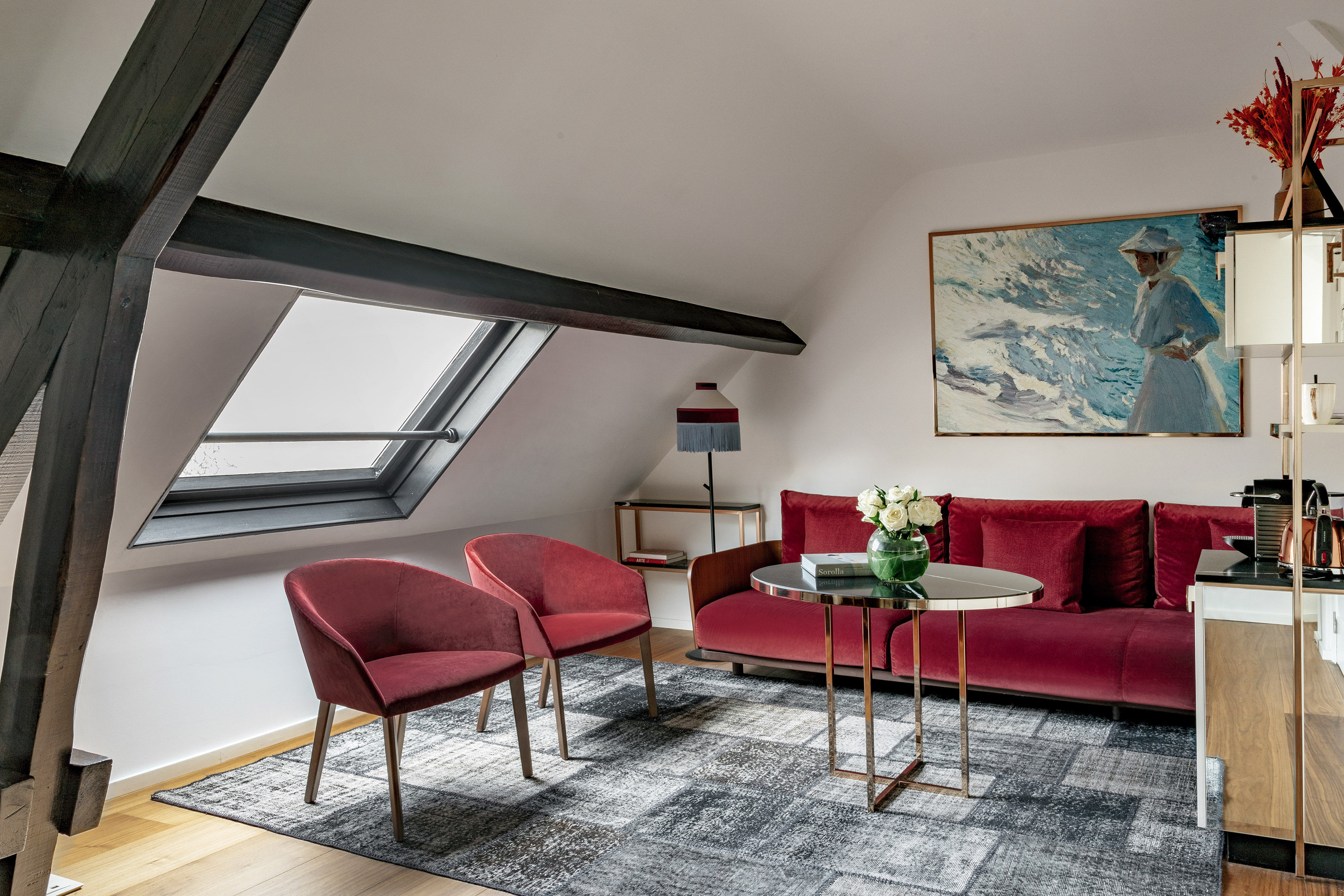 Attic living room with red velvet sofa, chairs, skylight, and exposed beams.
