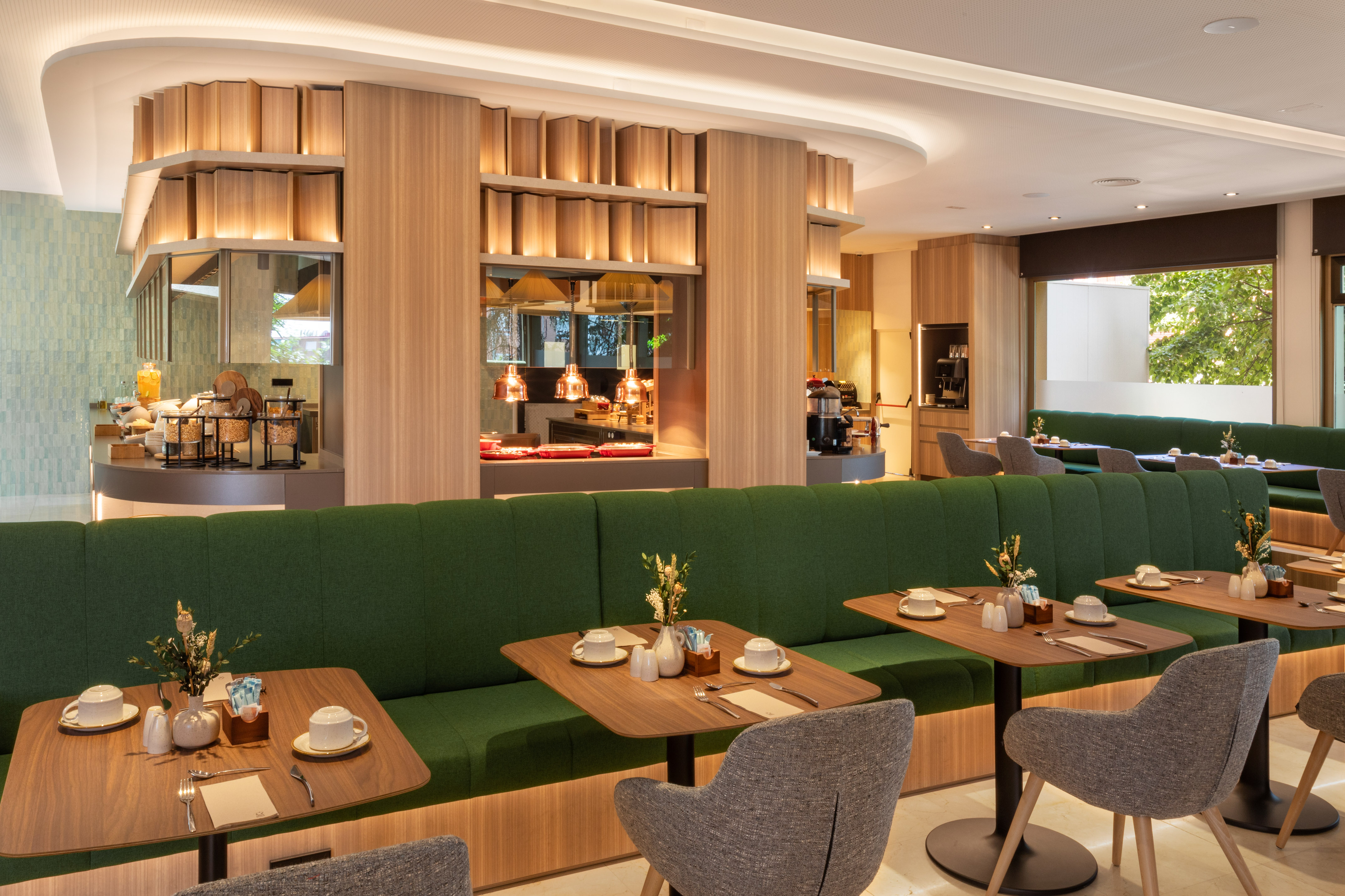 Modern breakfast buffet area with green banquettes and wooden tables.