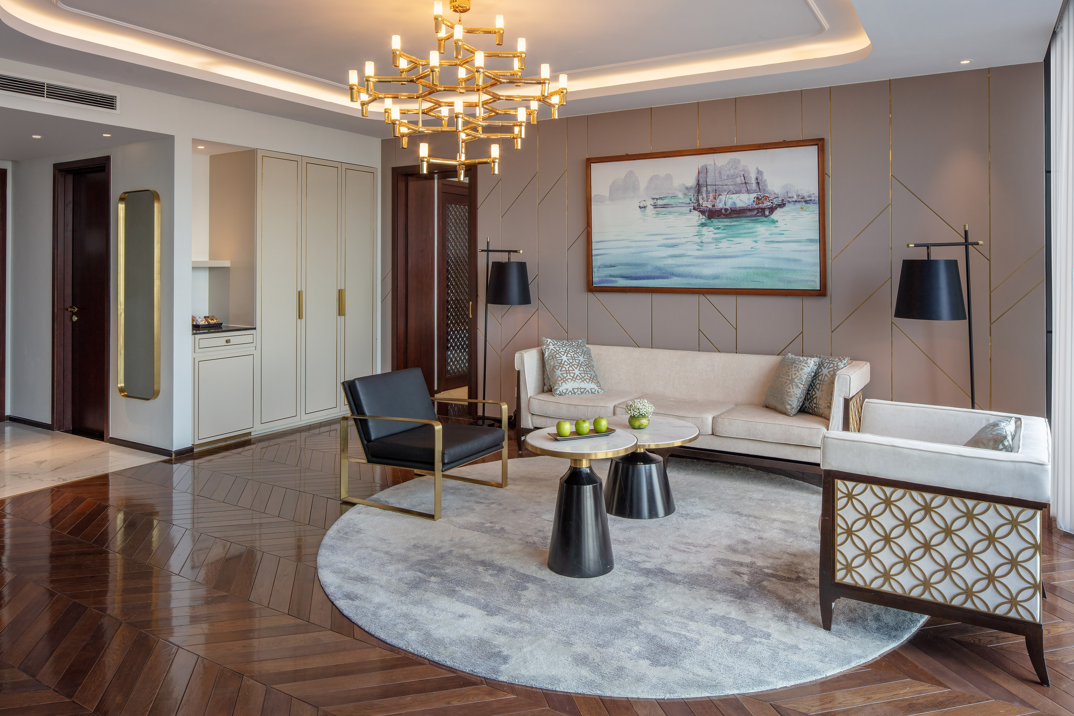Modern luxury living room, gold chandelier, cream sofa, dark wood floor, seascape art.