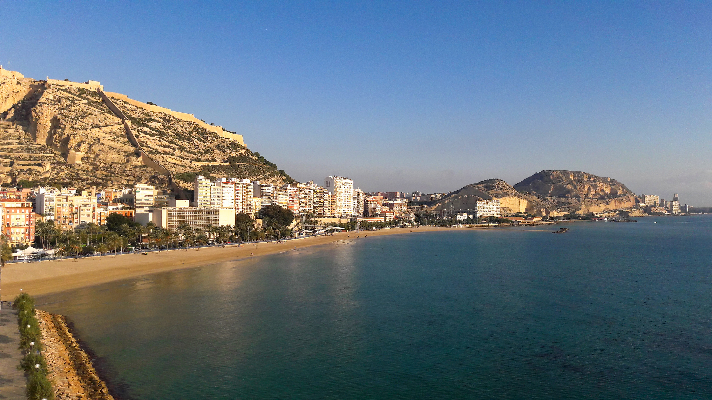 Alicante beach cityscape with Santa Bárbara Castle and blue sea.