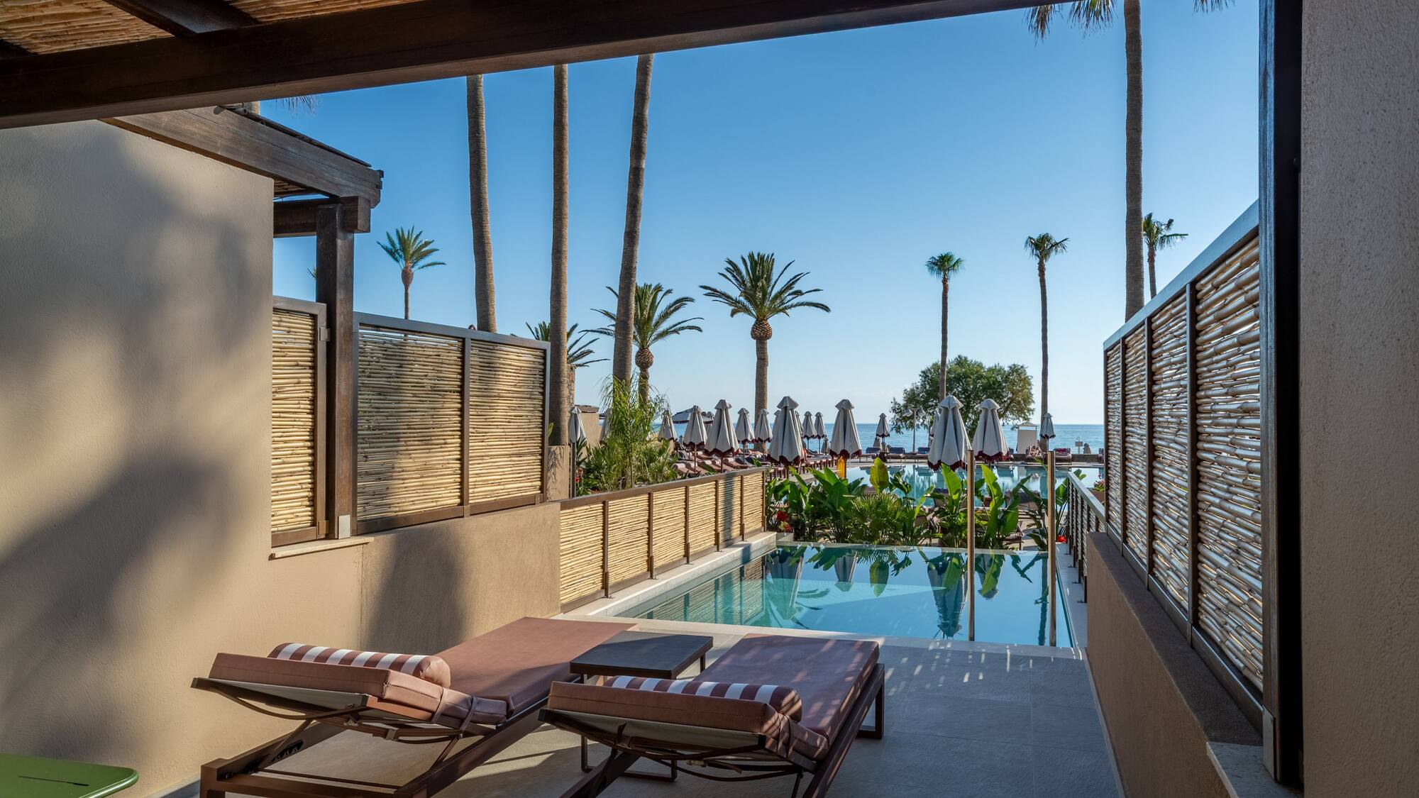 Resort patio with private pool, sun loungers, palm trees, and sea view.
