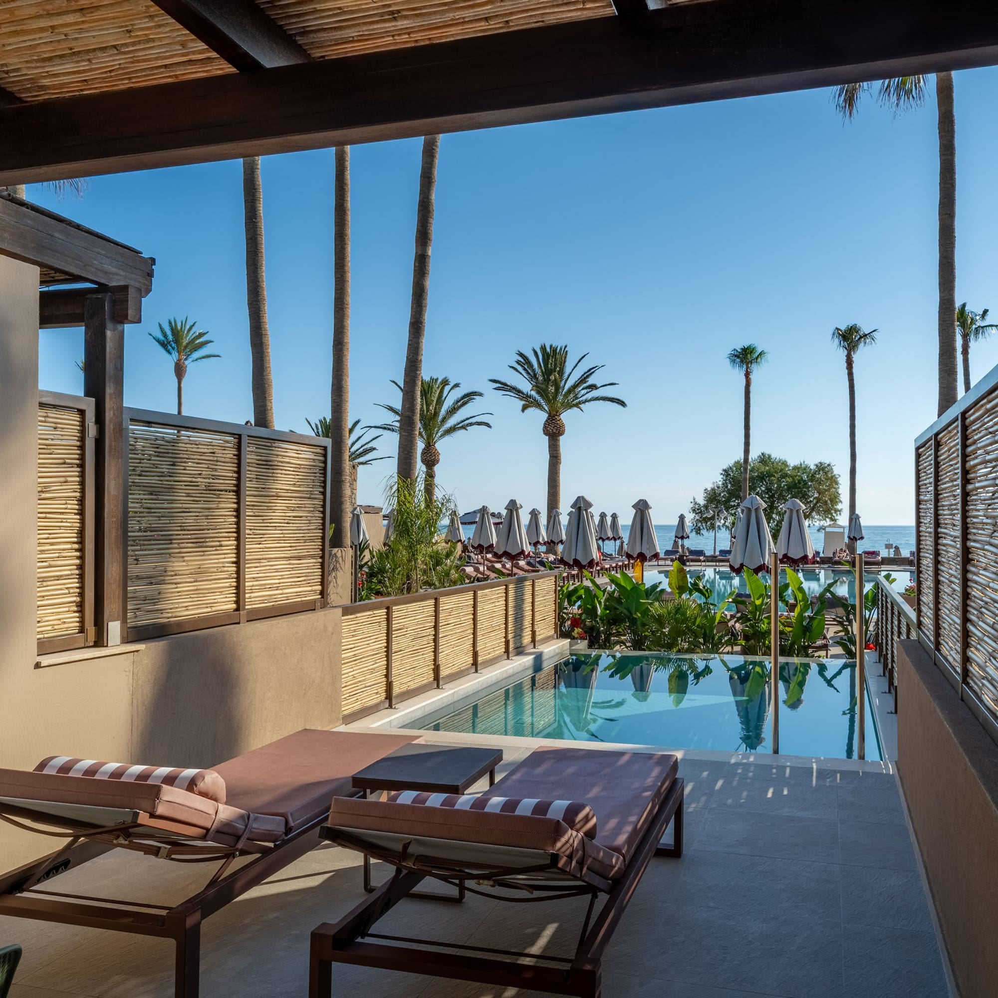 Resort patio with private pool, sun loungers, palm trees, and sea view.