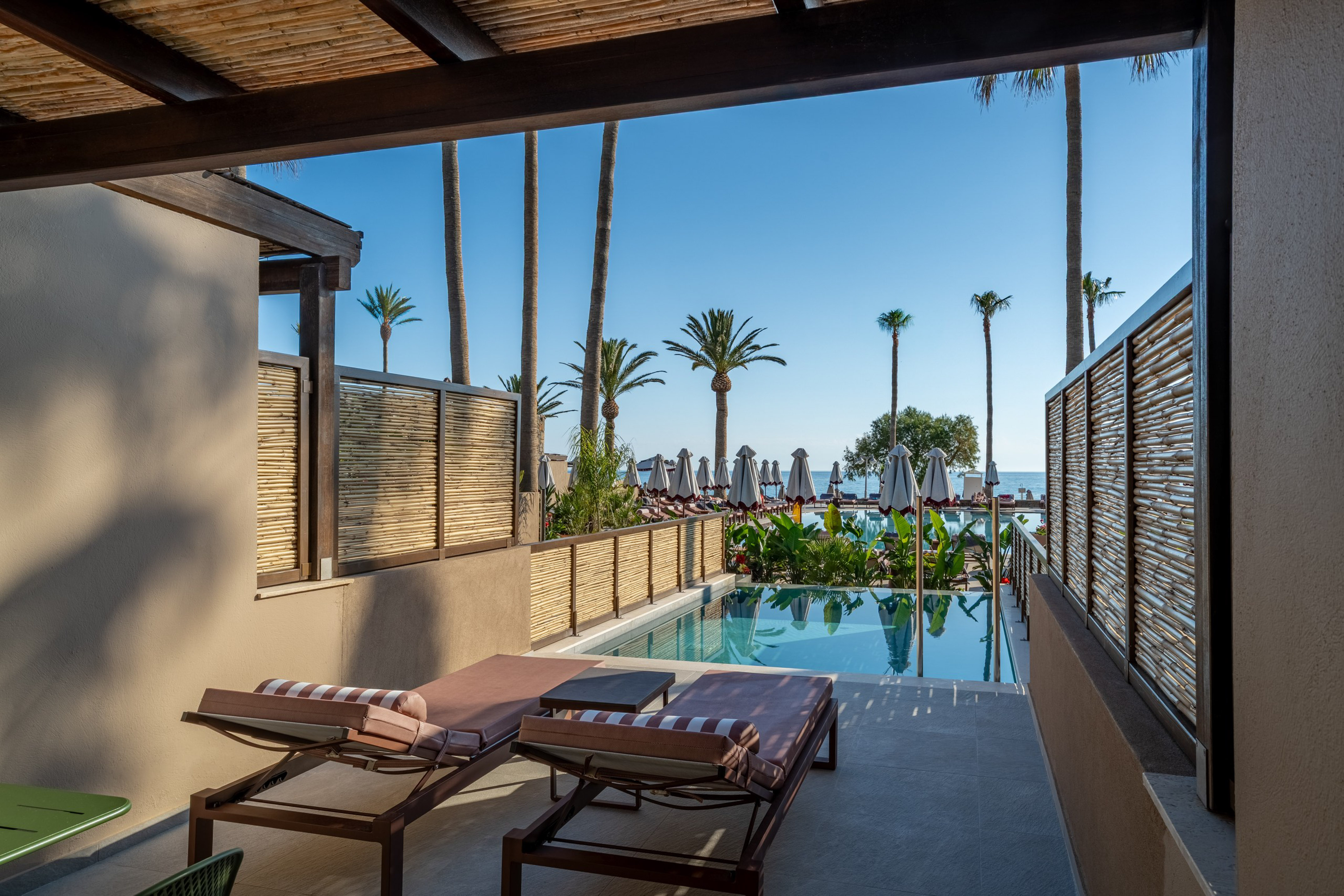 Resort patio with private pool, sun loungers, palm trees, and sea view.