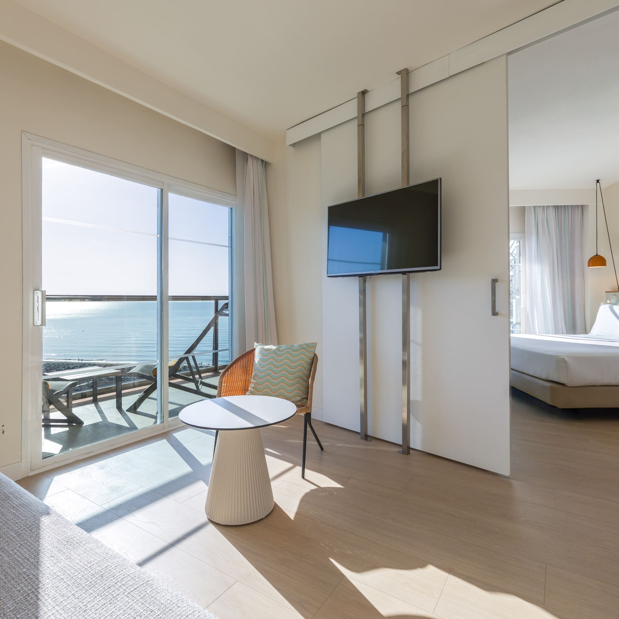 Bright hotel suite with ocean view balcony and sliding door to bedroom.