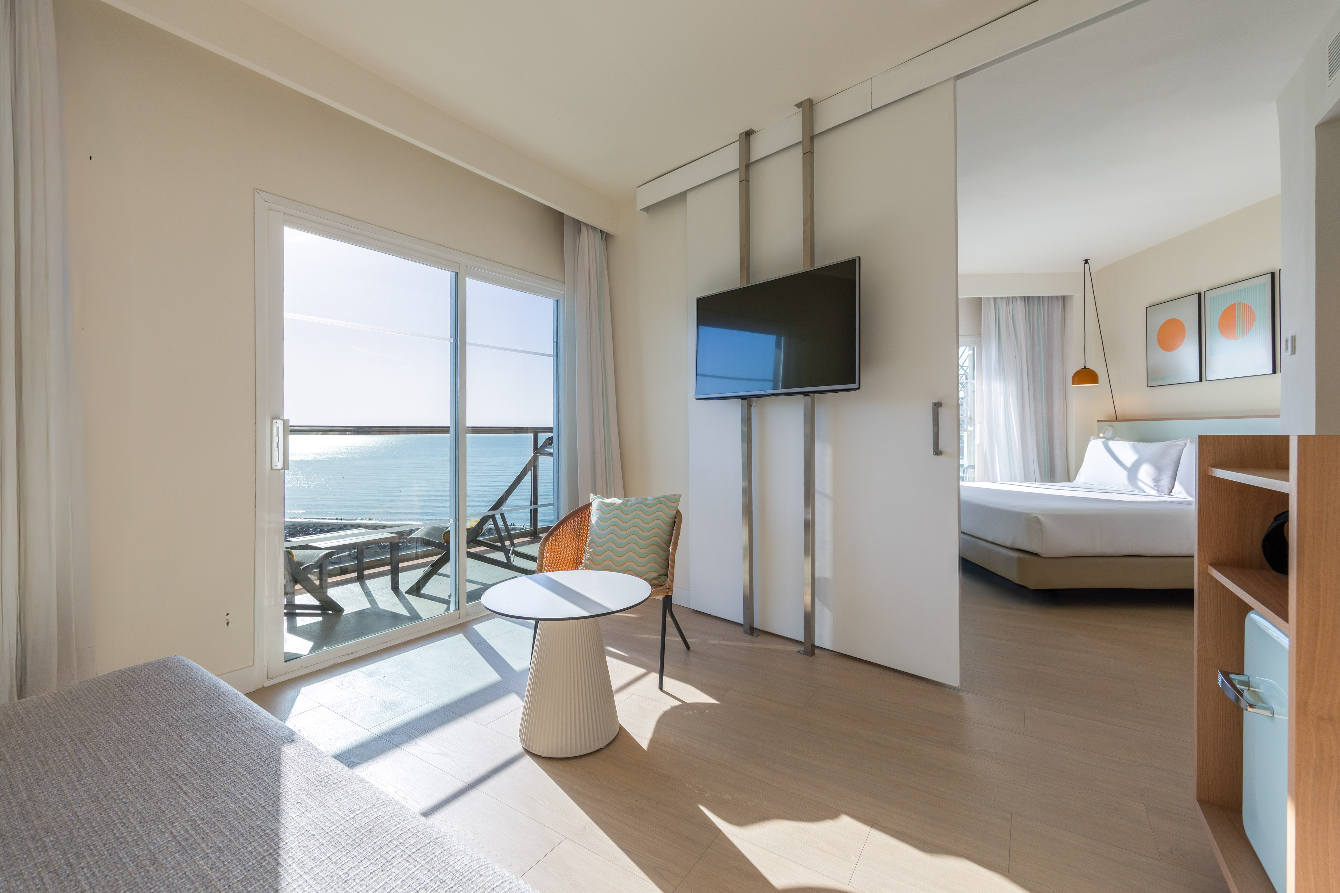 Modern hotel suite with ocean view balcony, living area, and bedroom.