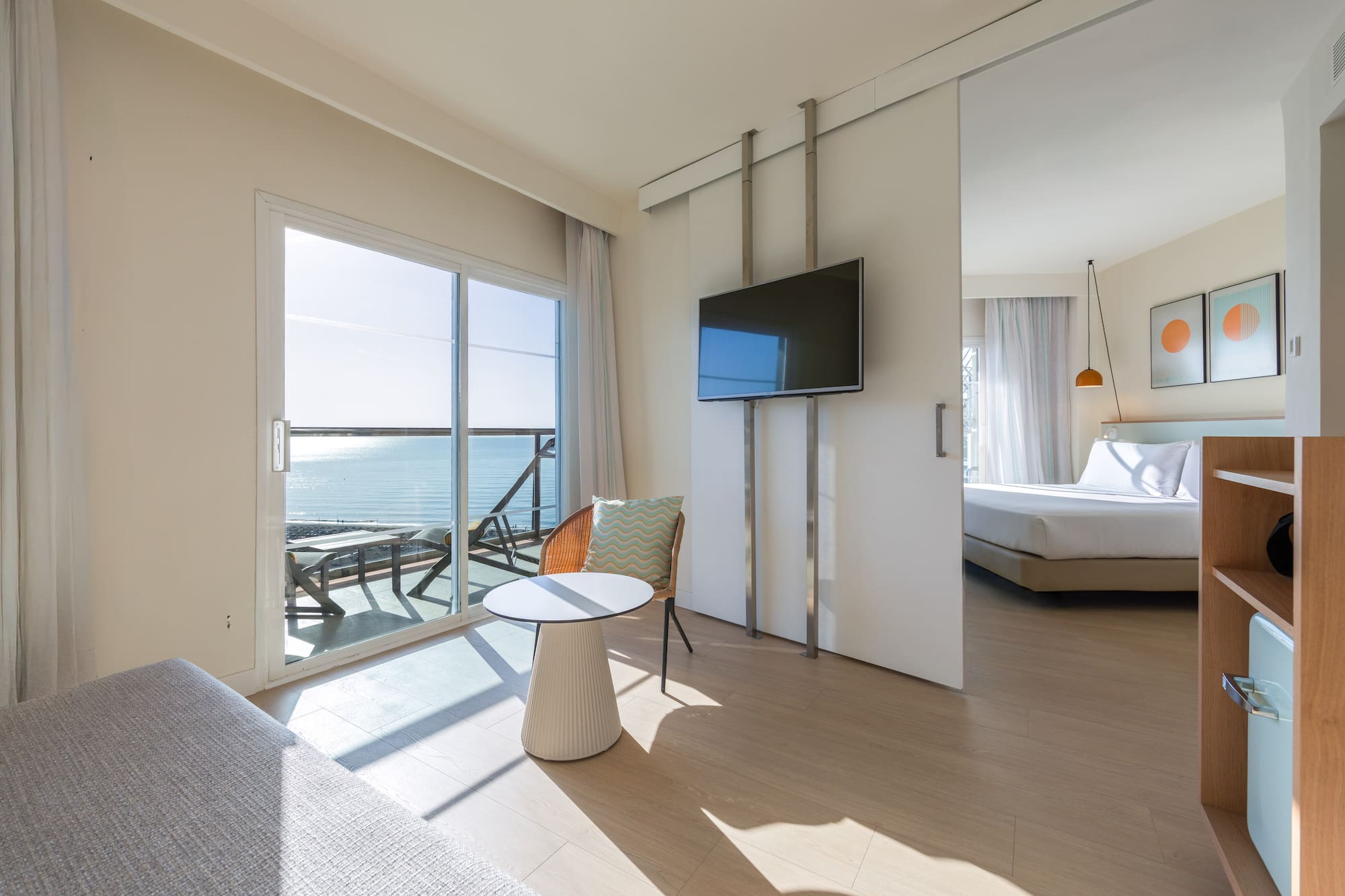 Modern hotel suite with ocean view balcony, living area, and bedroom.