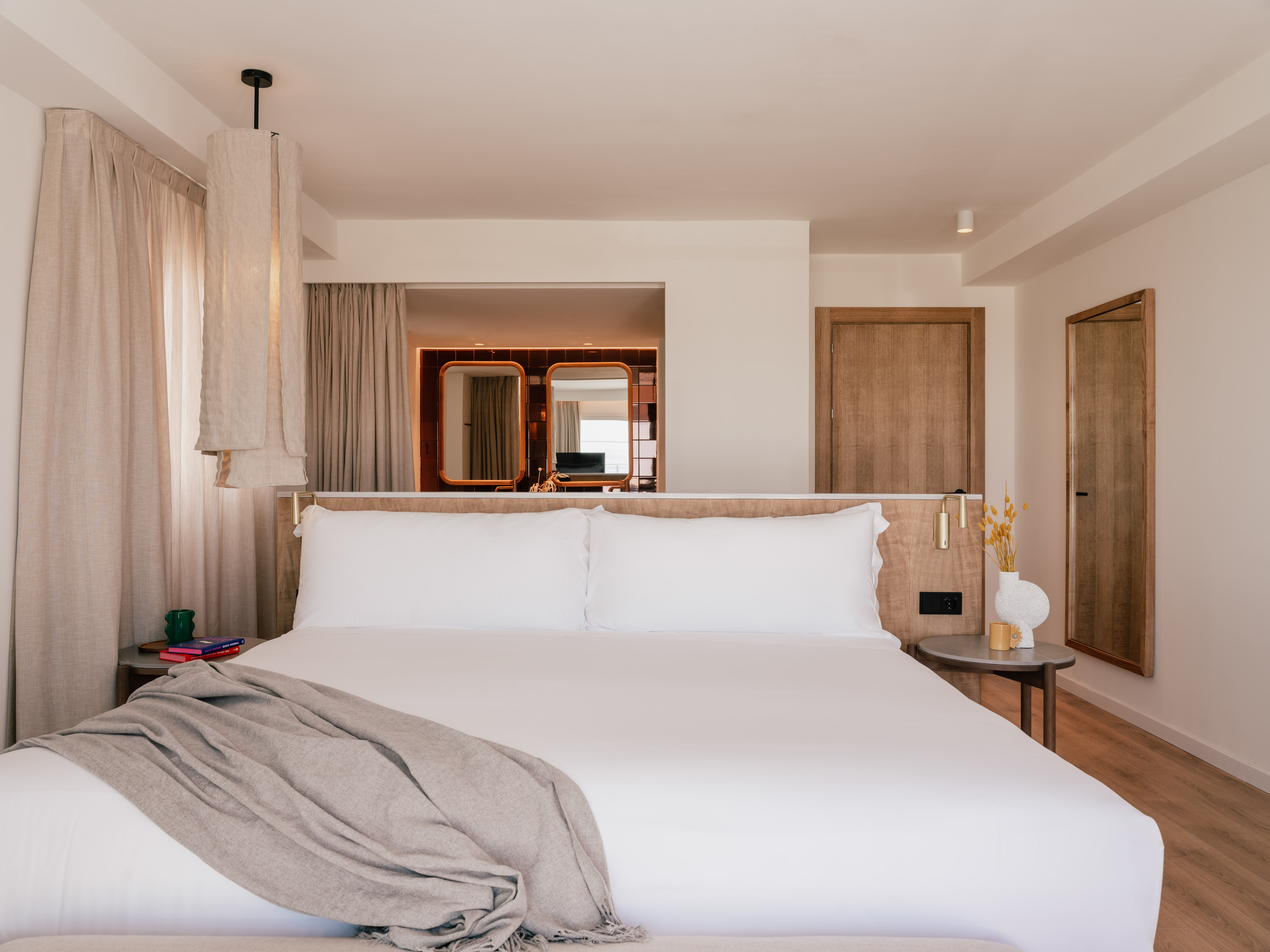 Modern hotel bedroom with king bed, white linens, wooden accents, and neutral decor.