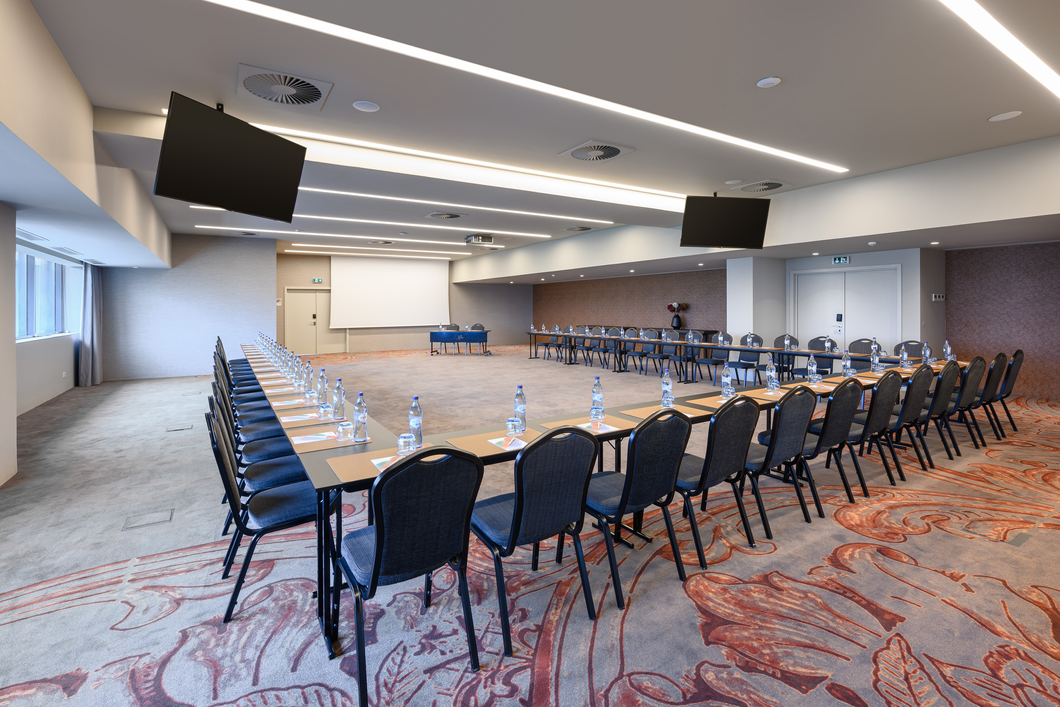 Modern U-shaped meeting room with tables, projector, and display screens.