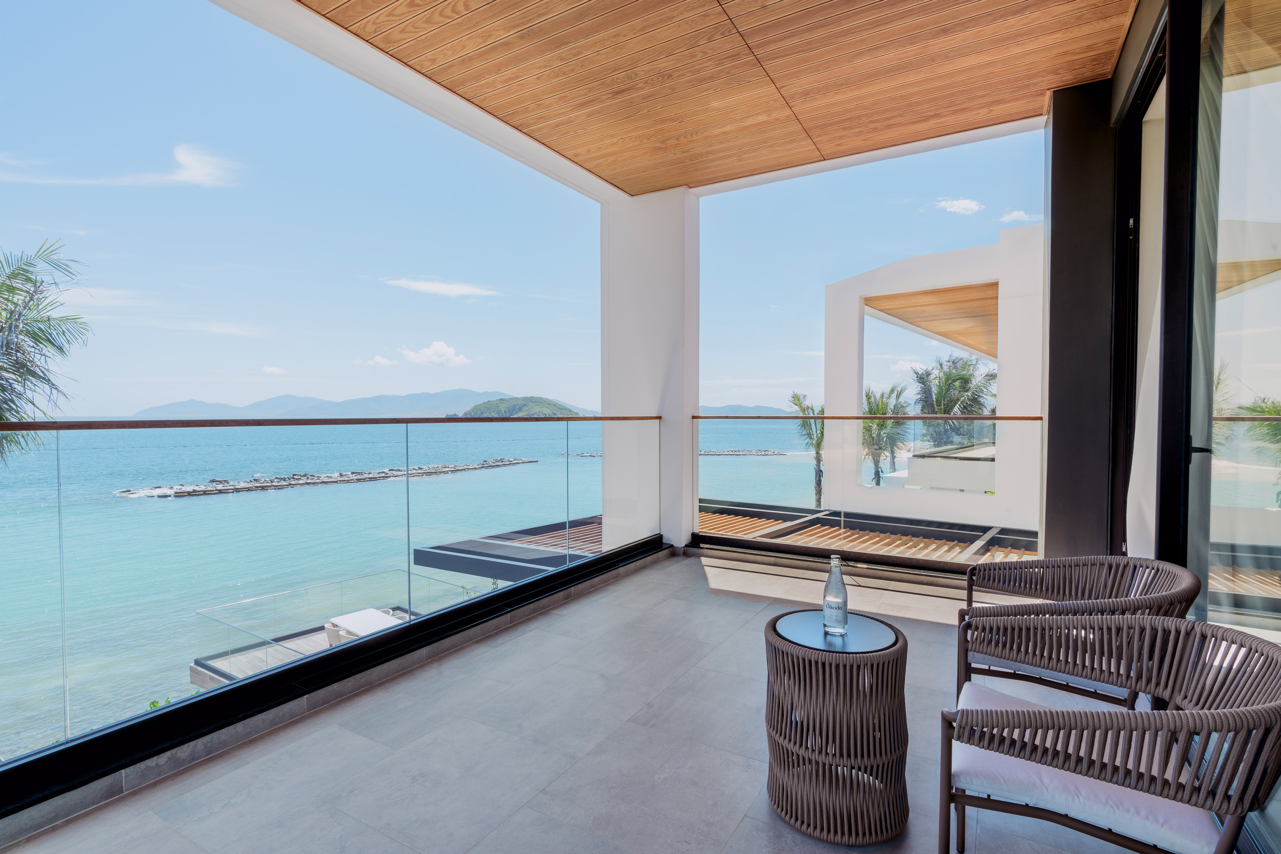 Luxury resort balcony with ocean view, outdoor chairs, and tropical palm trees.