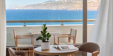 a table and chairs with a book on it by a window overlooking the ocean