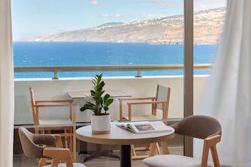 a table and chairs with a book on it by a window overlooking the ocean