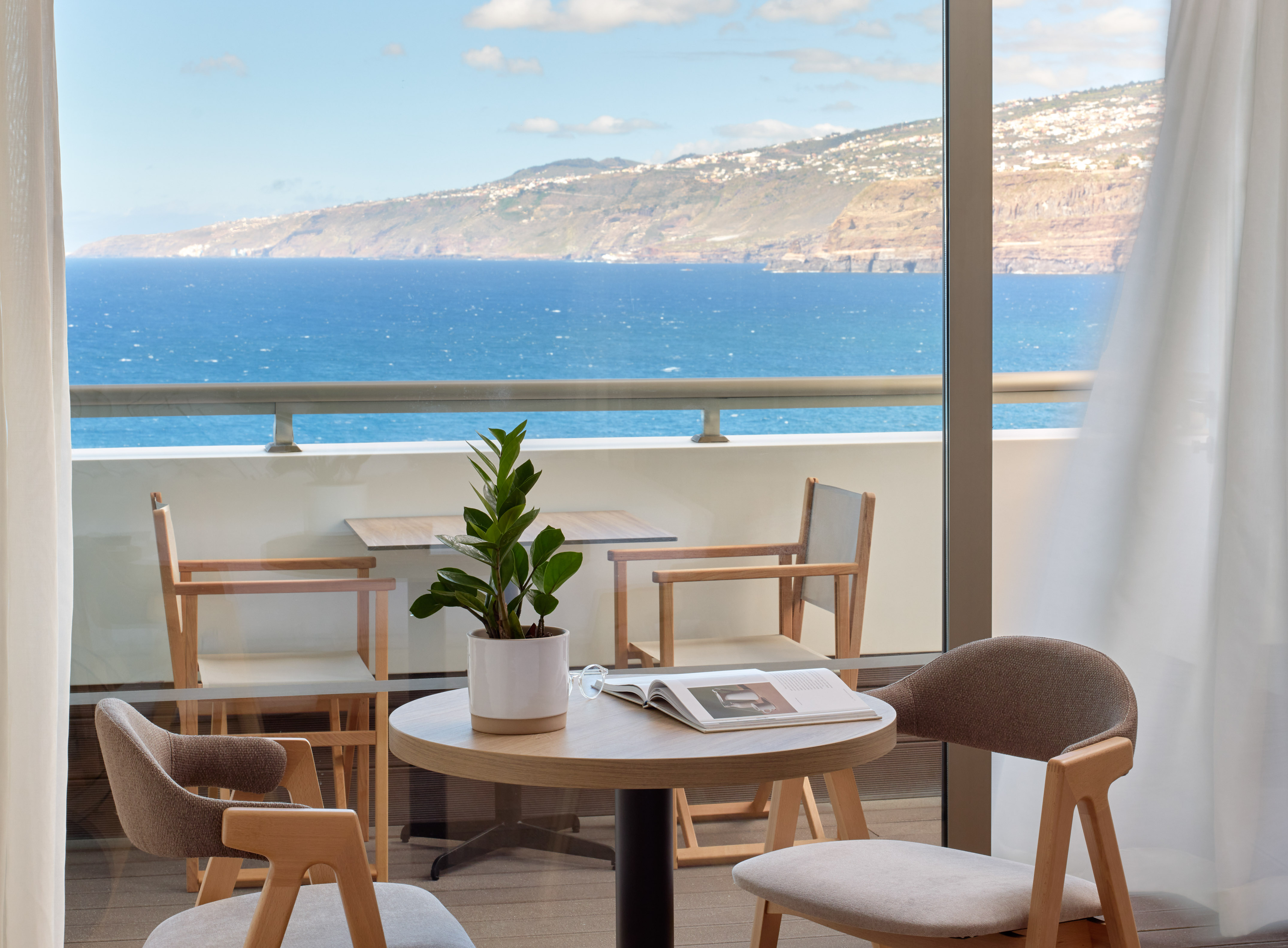 a table and chairs with a book on it by a window overlooking the ocean