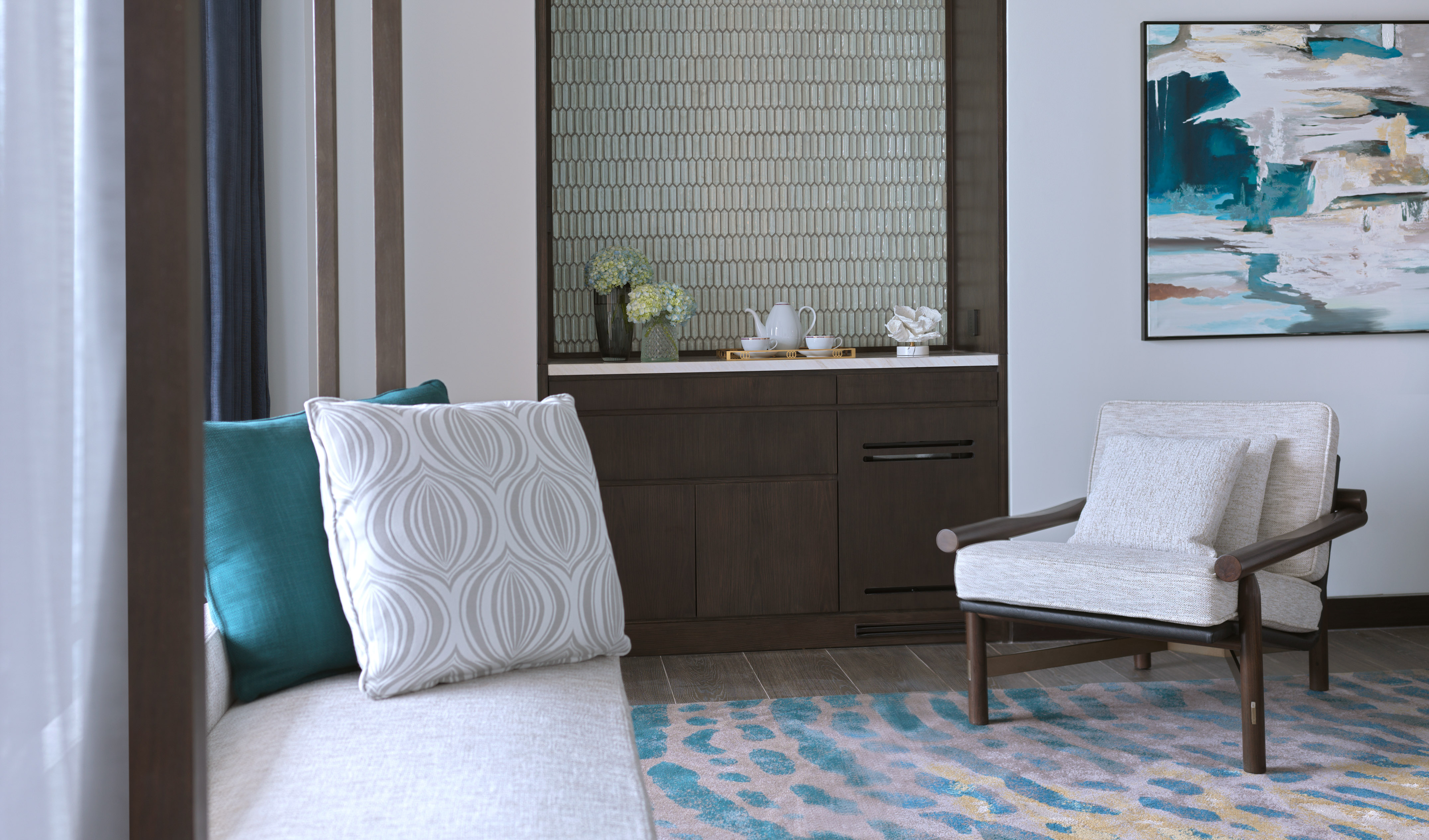 Modern hotel suite living area with sofa, accent chair, mini bar, and abstract art.