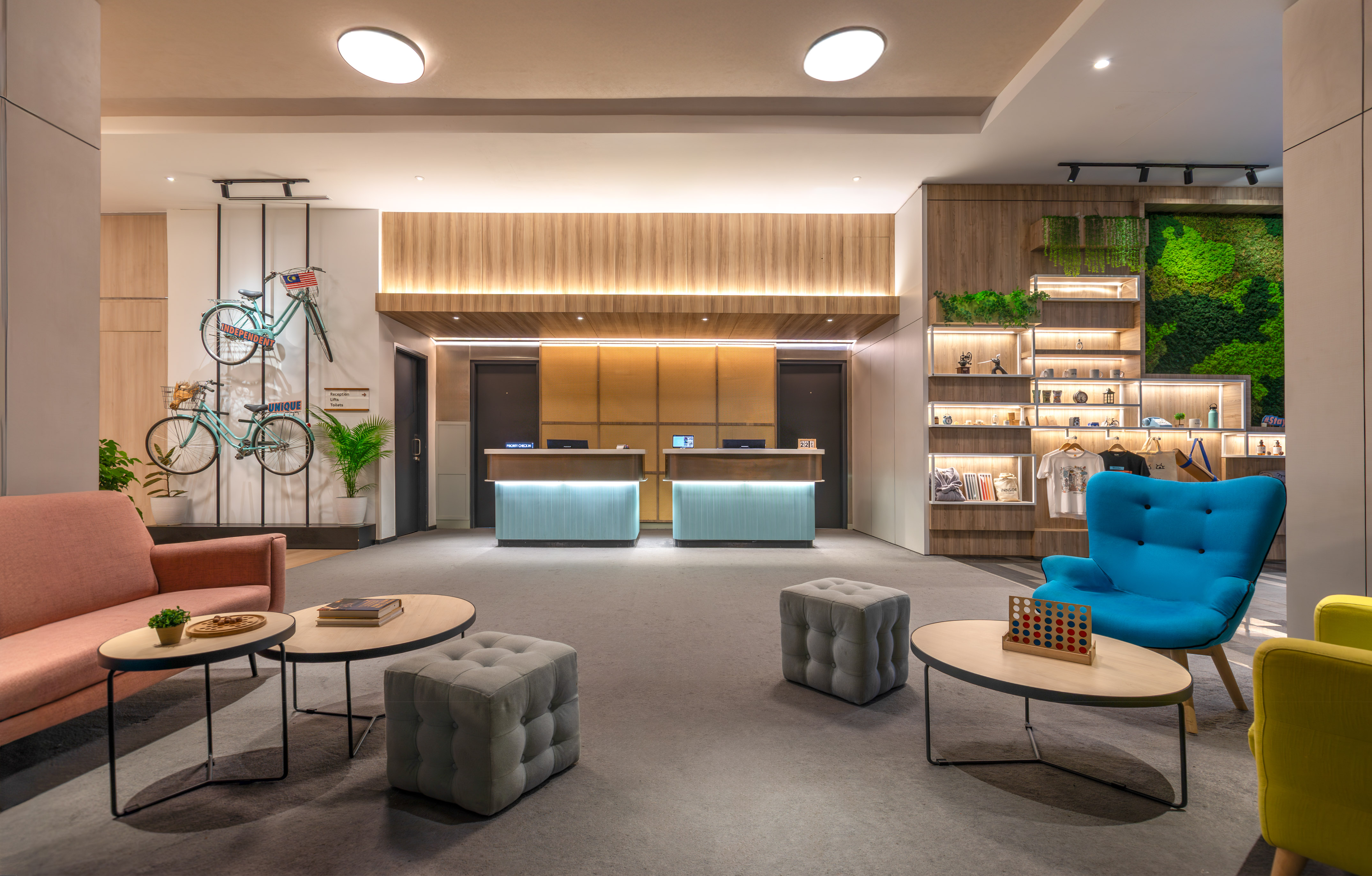 Modern hotel lobby with reception, lounge seating, bikes on wall, and moss art.