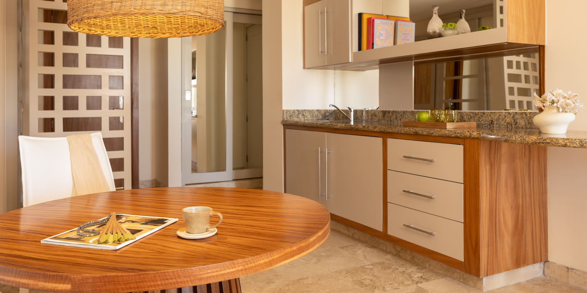 Modern dining area with round wood table, wicker light, and kitchenette.