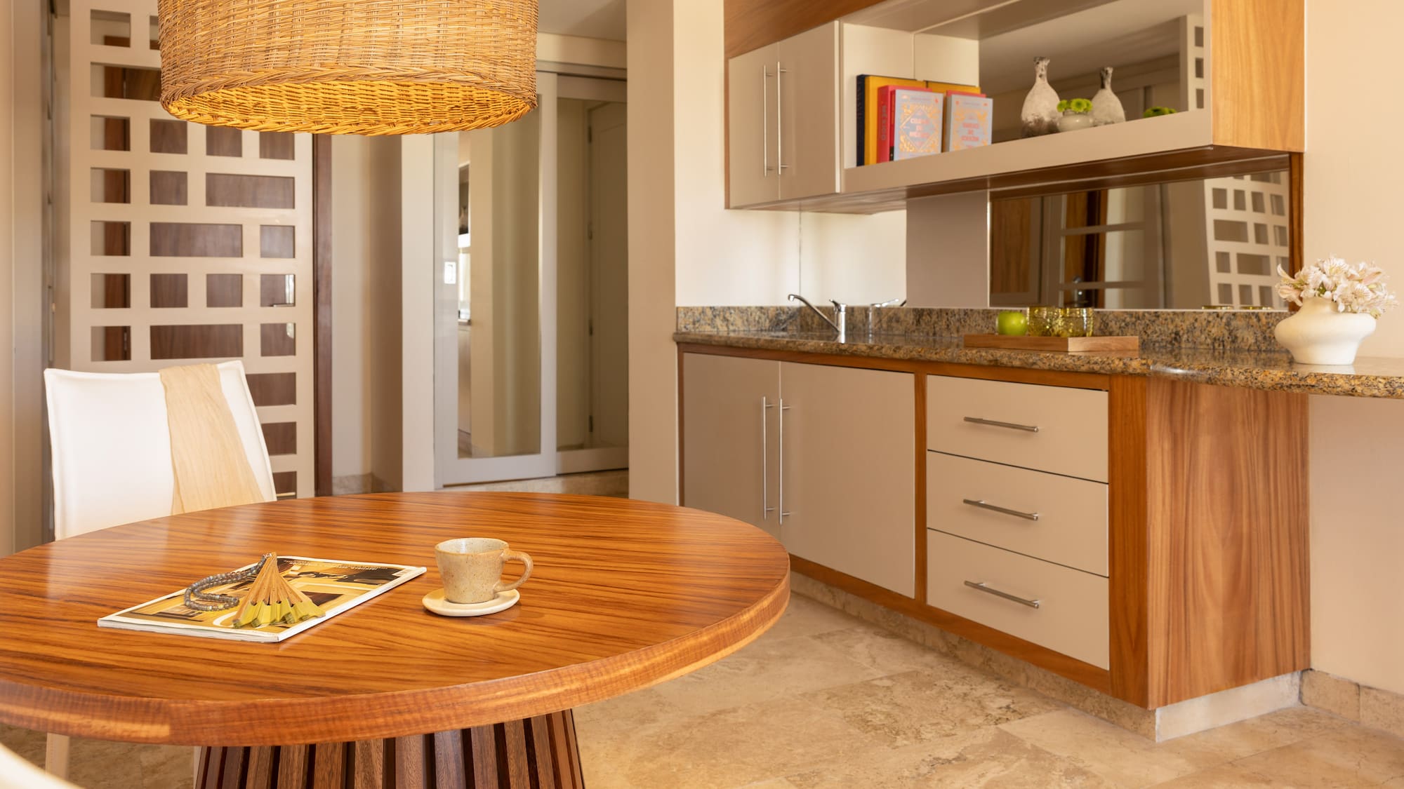 Modern dining area with round wood table, wicker light, and kitchenette.