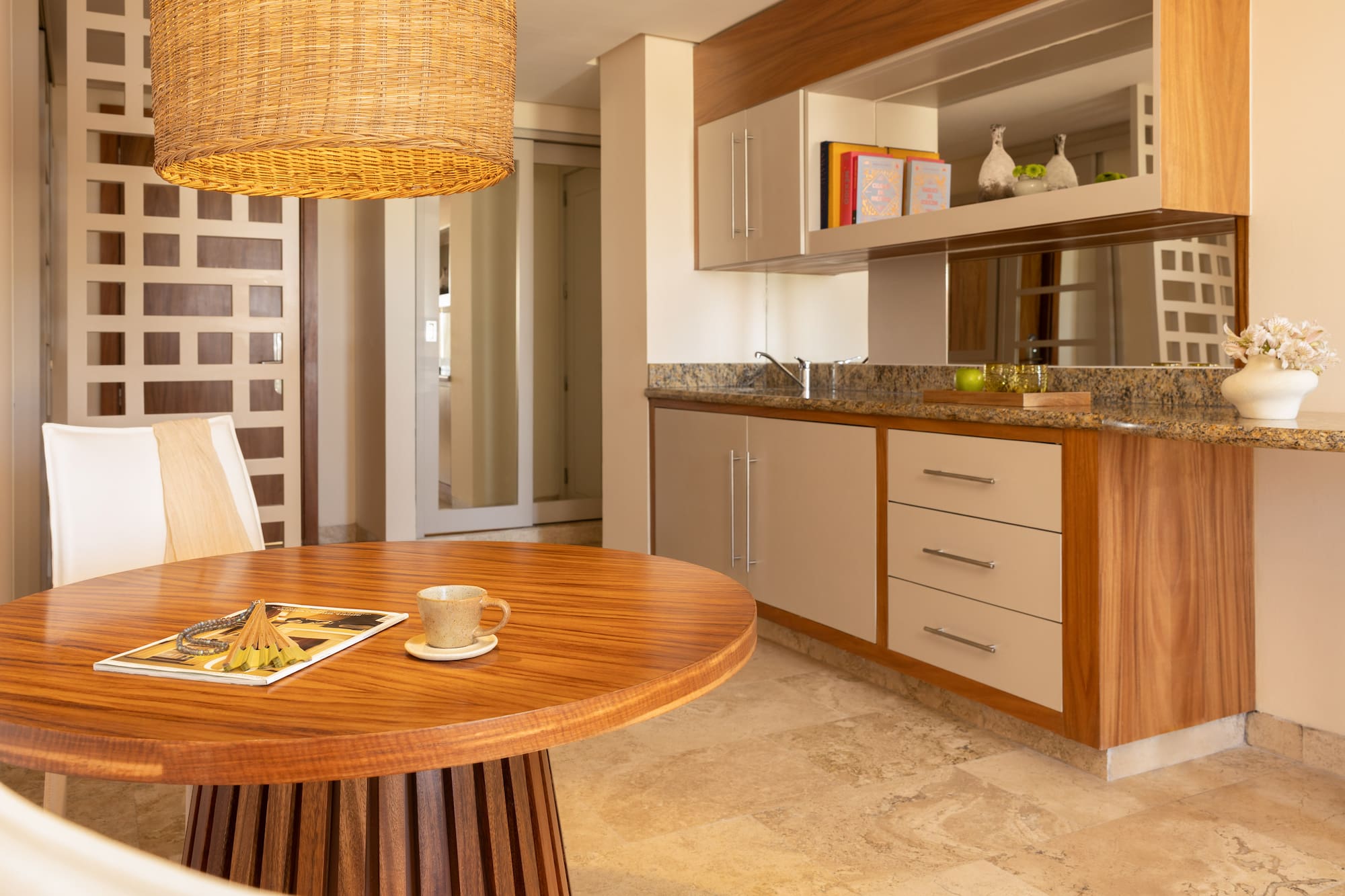 Modern dining area with round wood table, wicker light, and kitchenette.