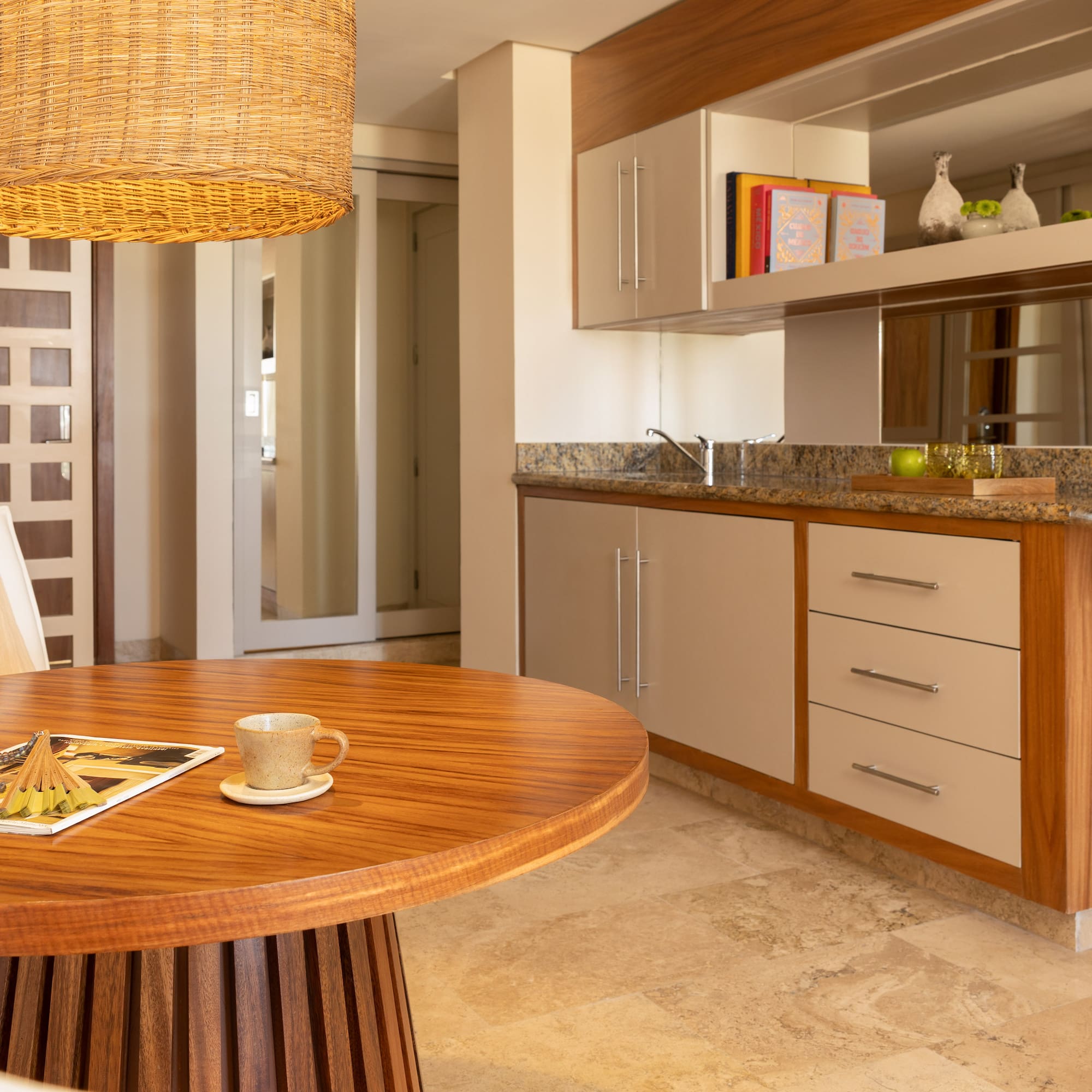 Modern dining area with round wood table, wicker light, and kitchenette.