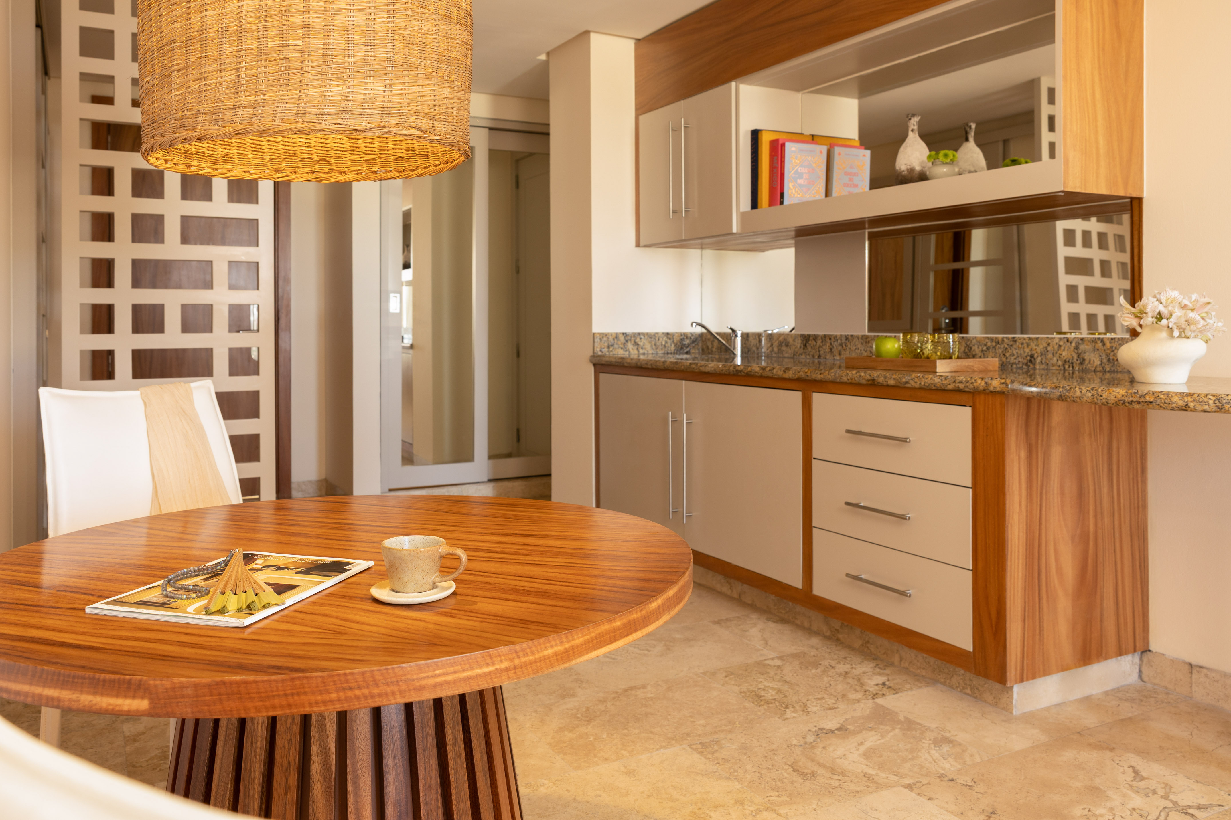 Modern dining area with round wood table, wicker light, and kitchenette.