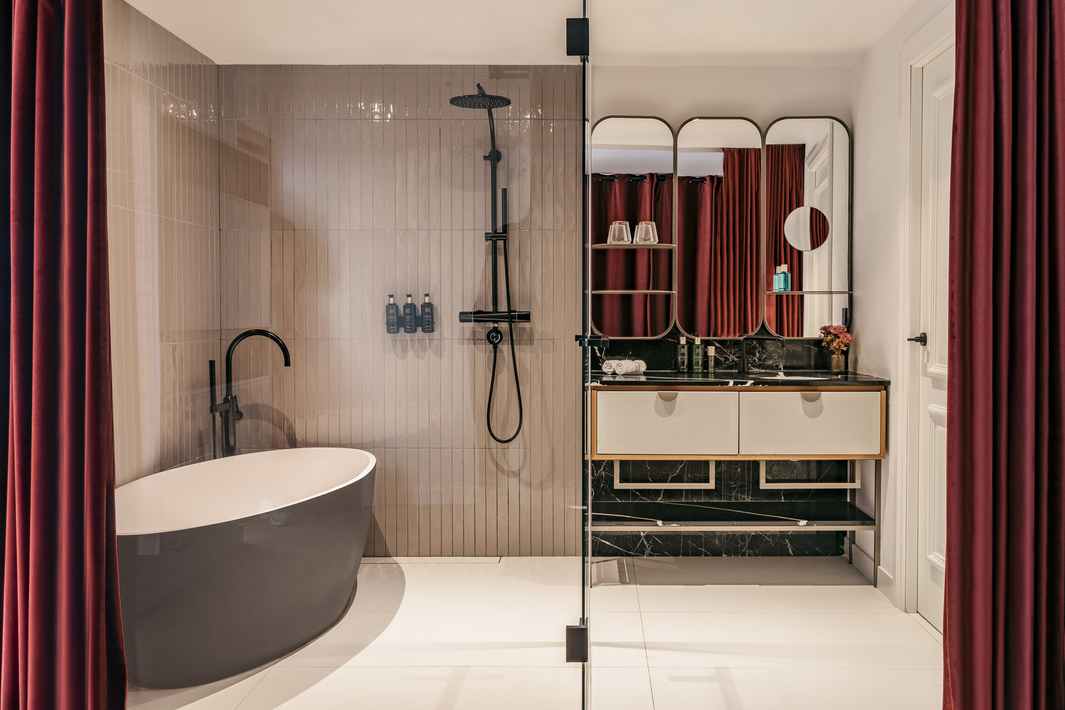 Freestanding tub and shower in a modern bathroom with red curtains and vanity.