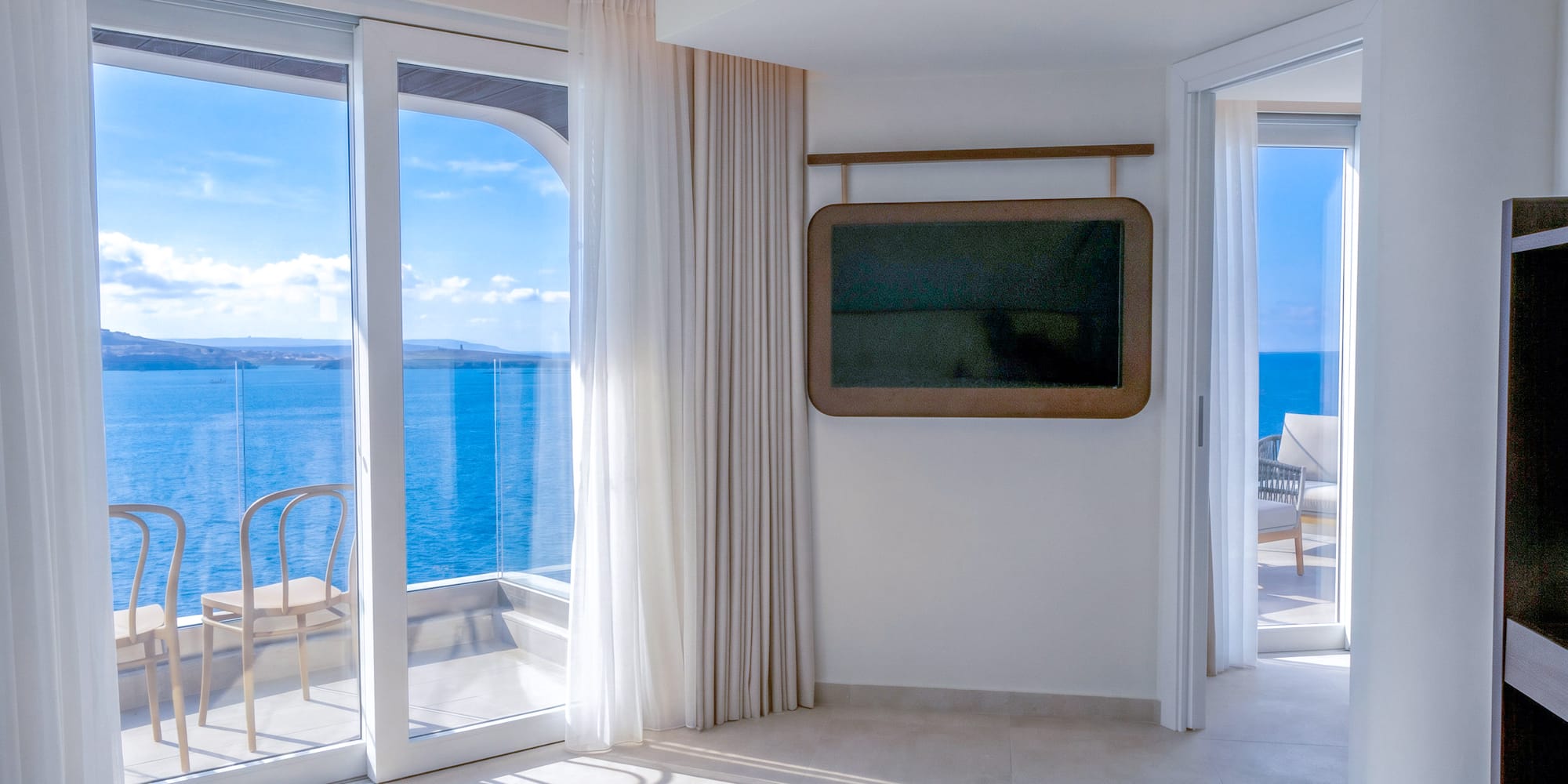 Modern hotel room with balcony, sea view, and wall-mounted TV.