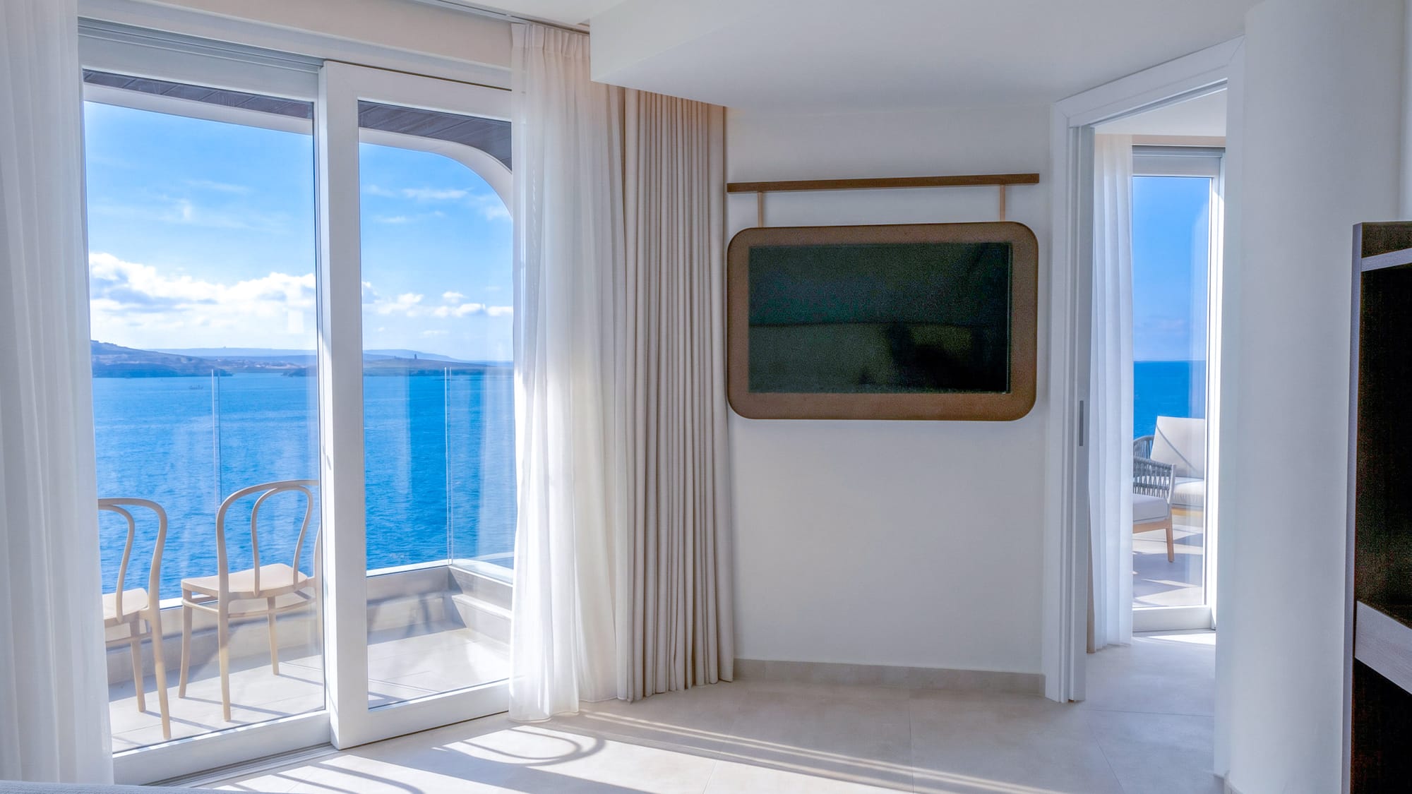 Modern hotel room with balcony, sea view, and wall-mounted TV.