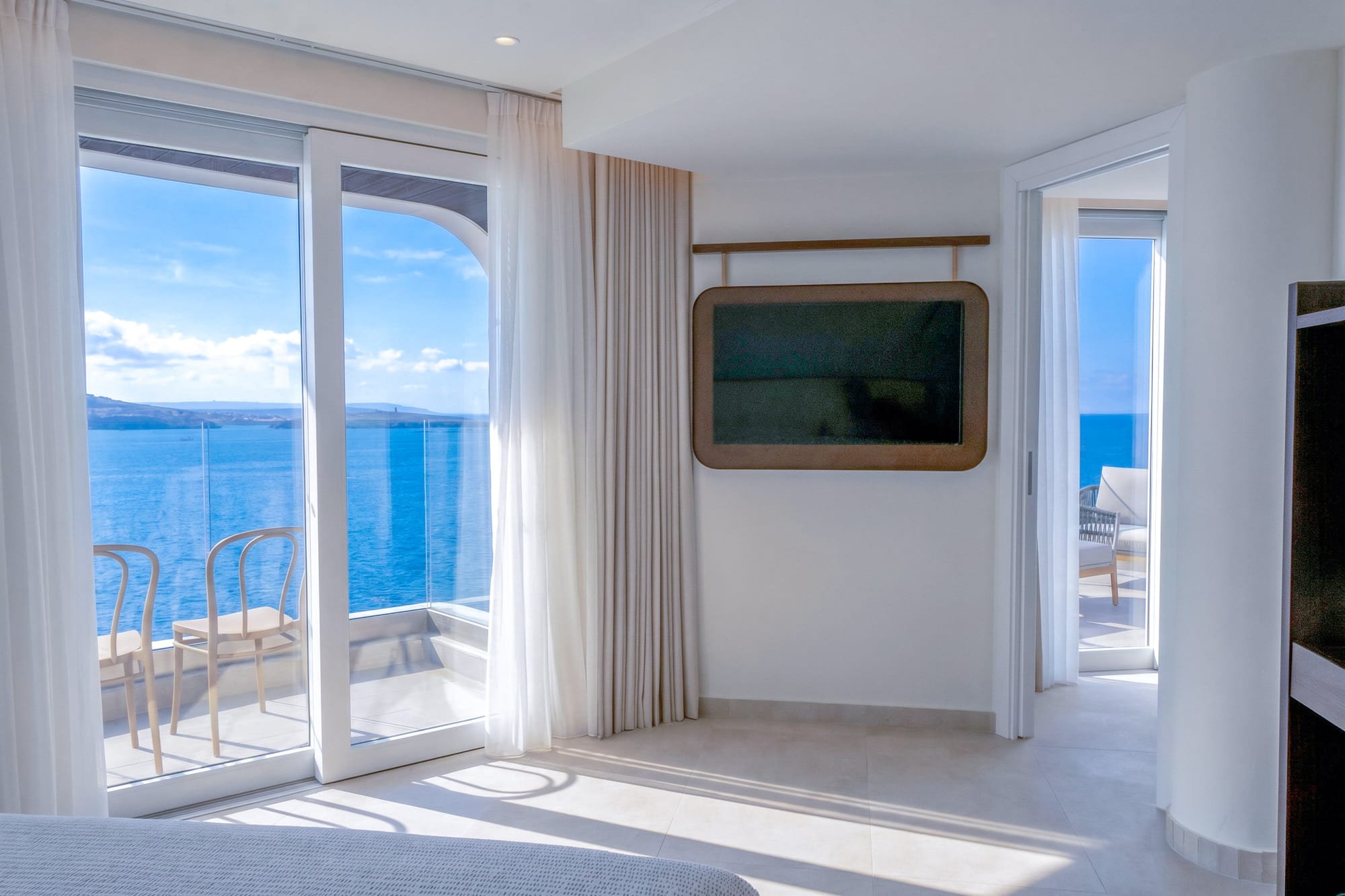 Modern hotel room with balcony, sea view, and wall-mounted TV.