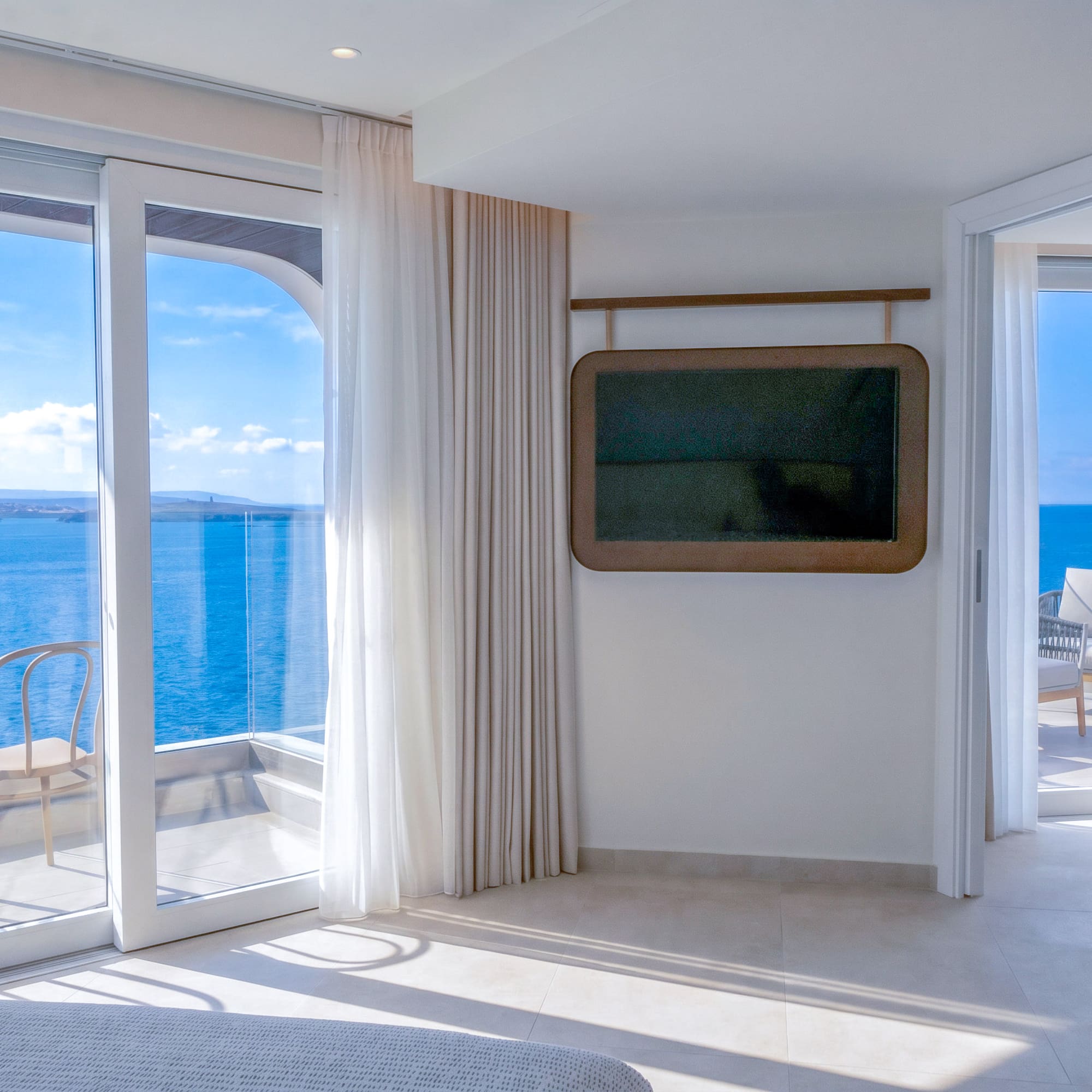 Modern hotel room with balcony, sea view, and wall-mounted TV.