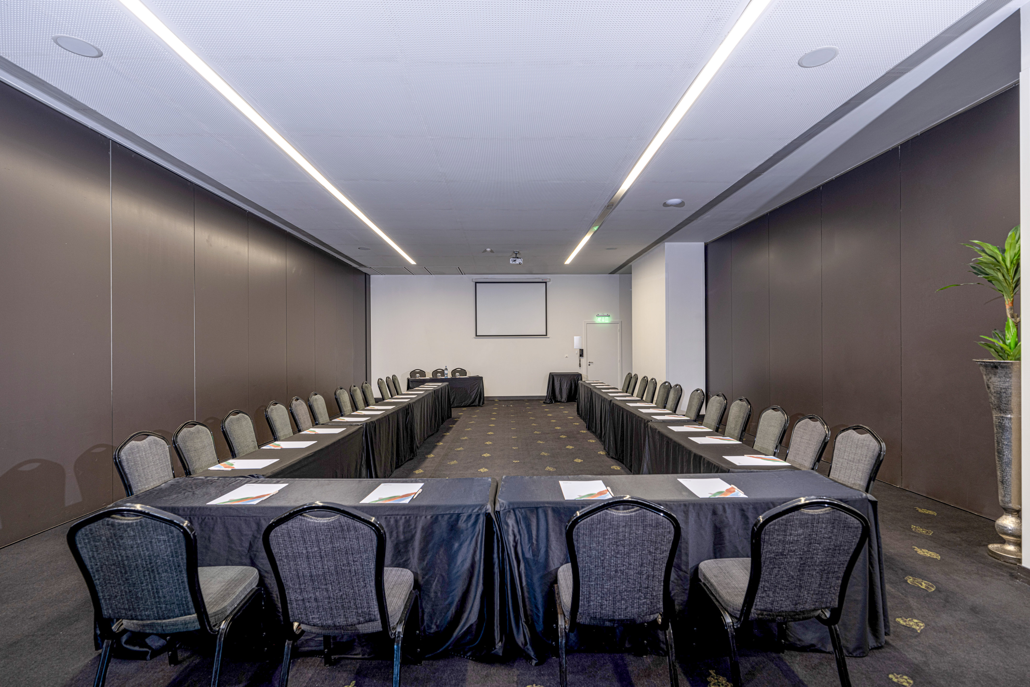 U-shape conference room with black tables, grey chairs, and projector screen.