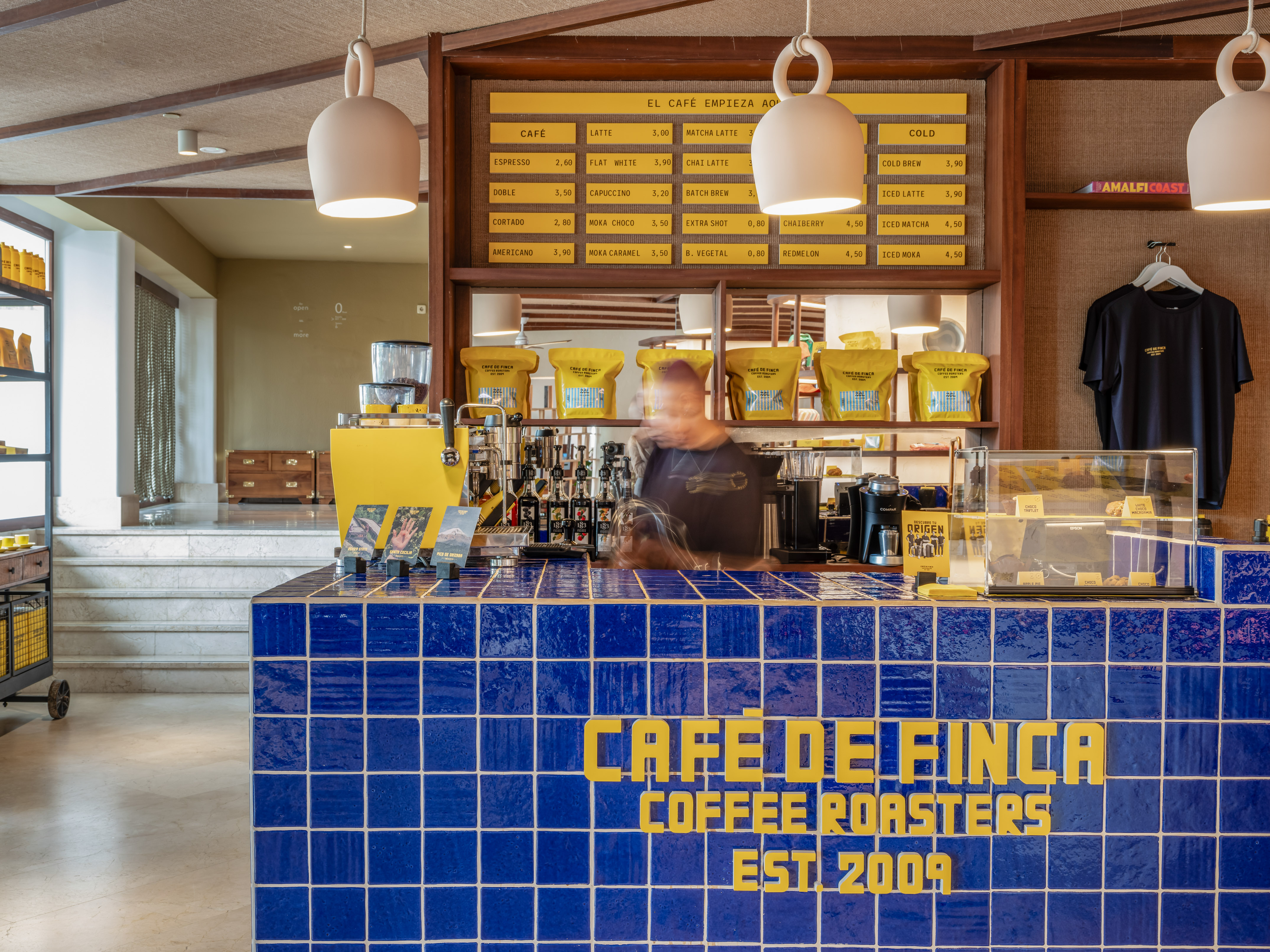 Cafe de Finca coffee bar with blue tiles, yellow branding, and coffee menu.