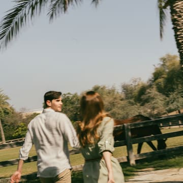 a man and woman walking by a fence and palm trees