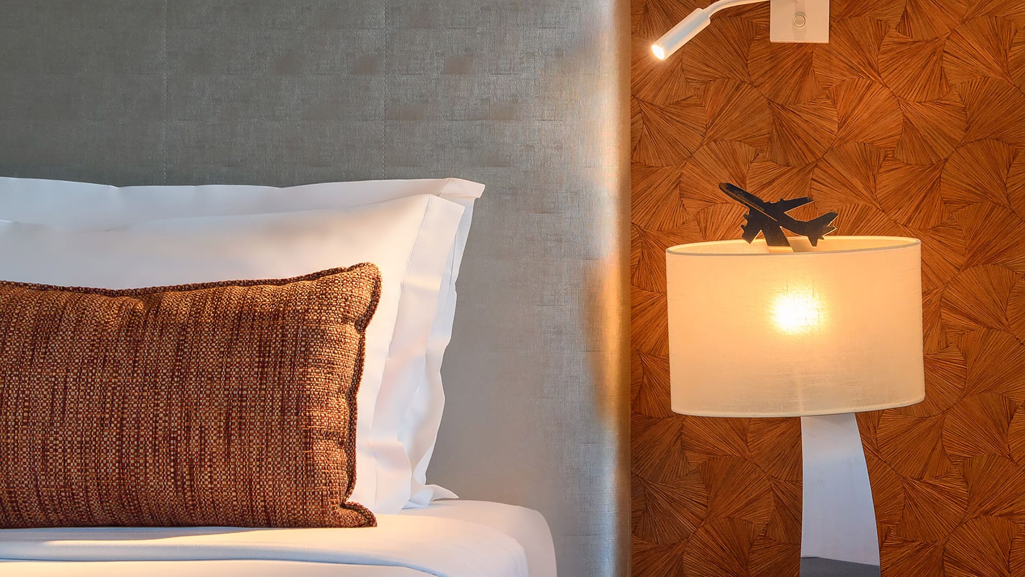 Modern bedroom: gray headboard, bedside table with airplane lamp, textured wall.