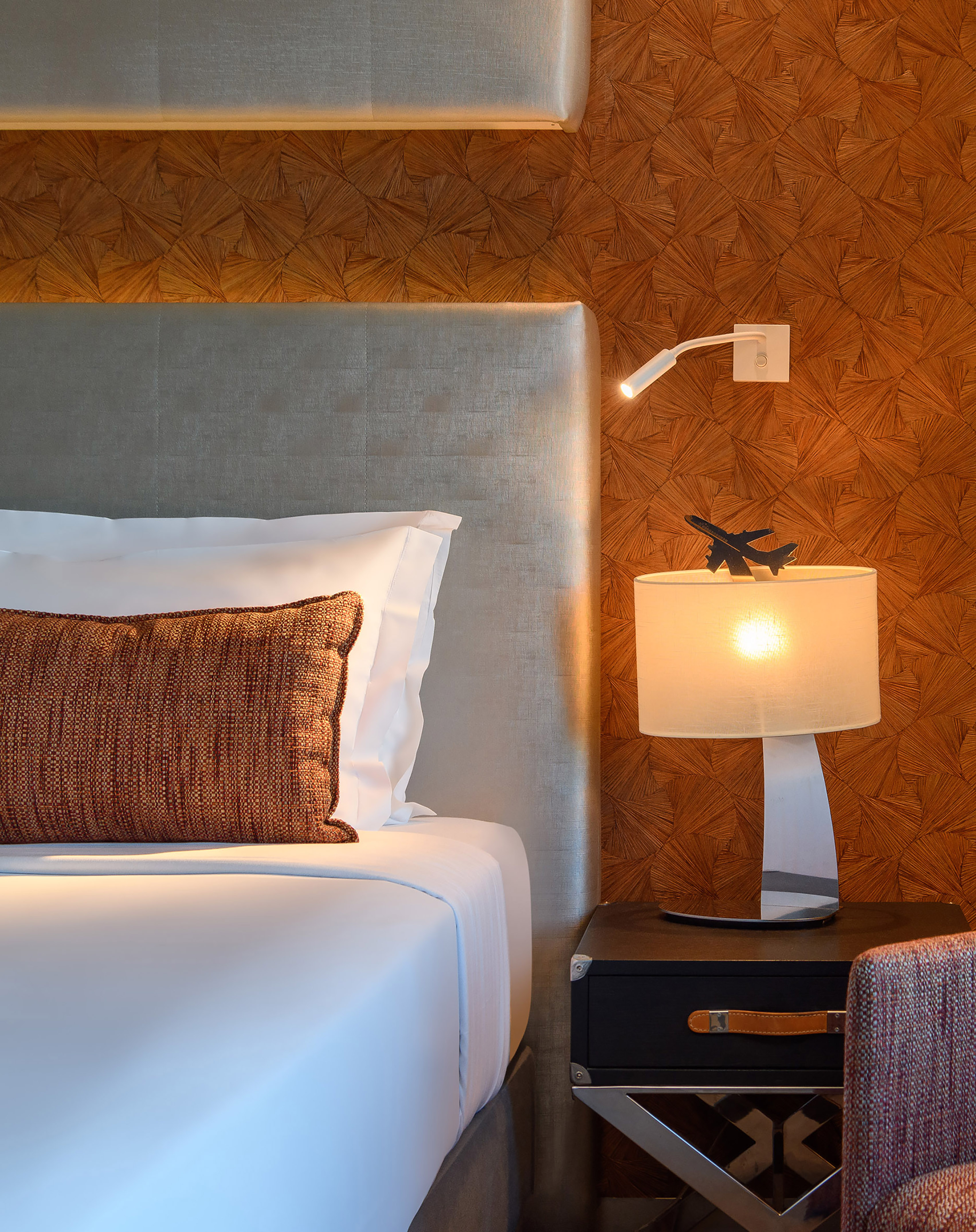 Modern bedroom: gray headboard, bedside table with airplane lamp, textured wall.