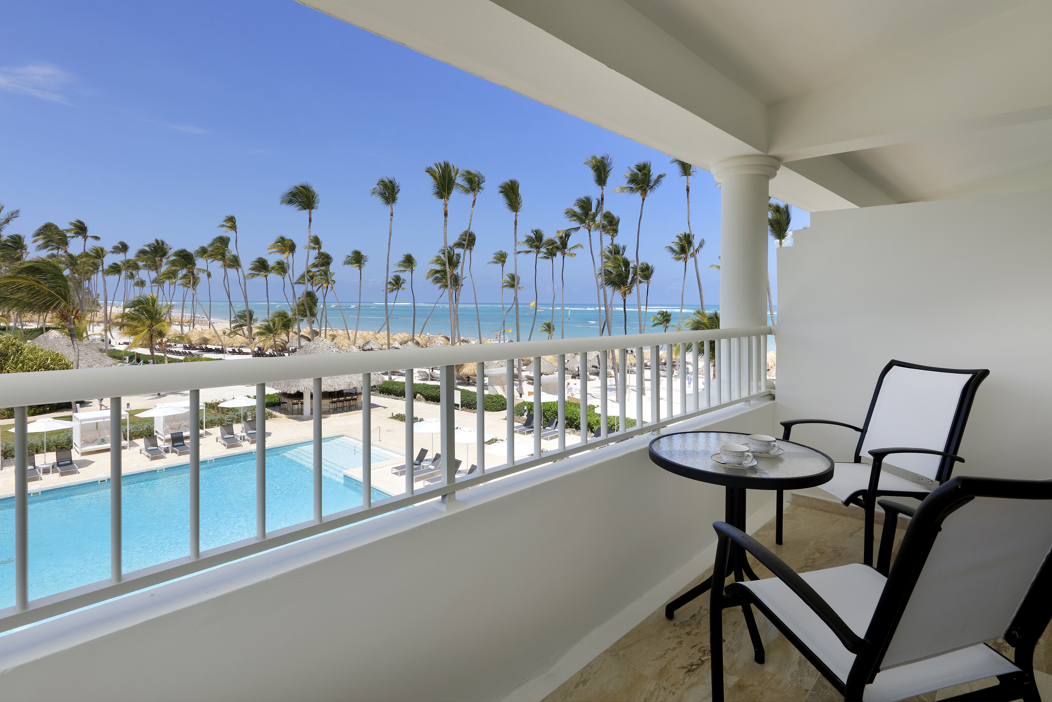 Balcony view of tropical resort, pool, sandy beach, palm trees, and ocean.