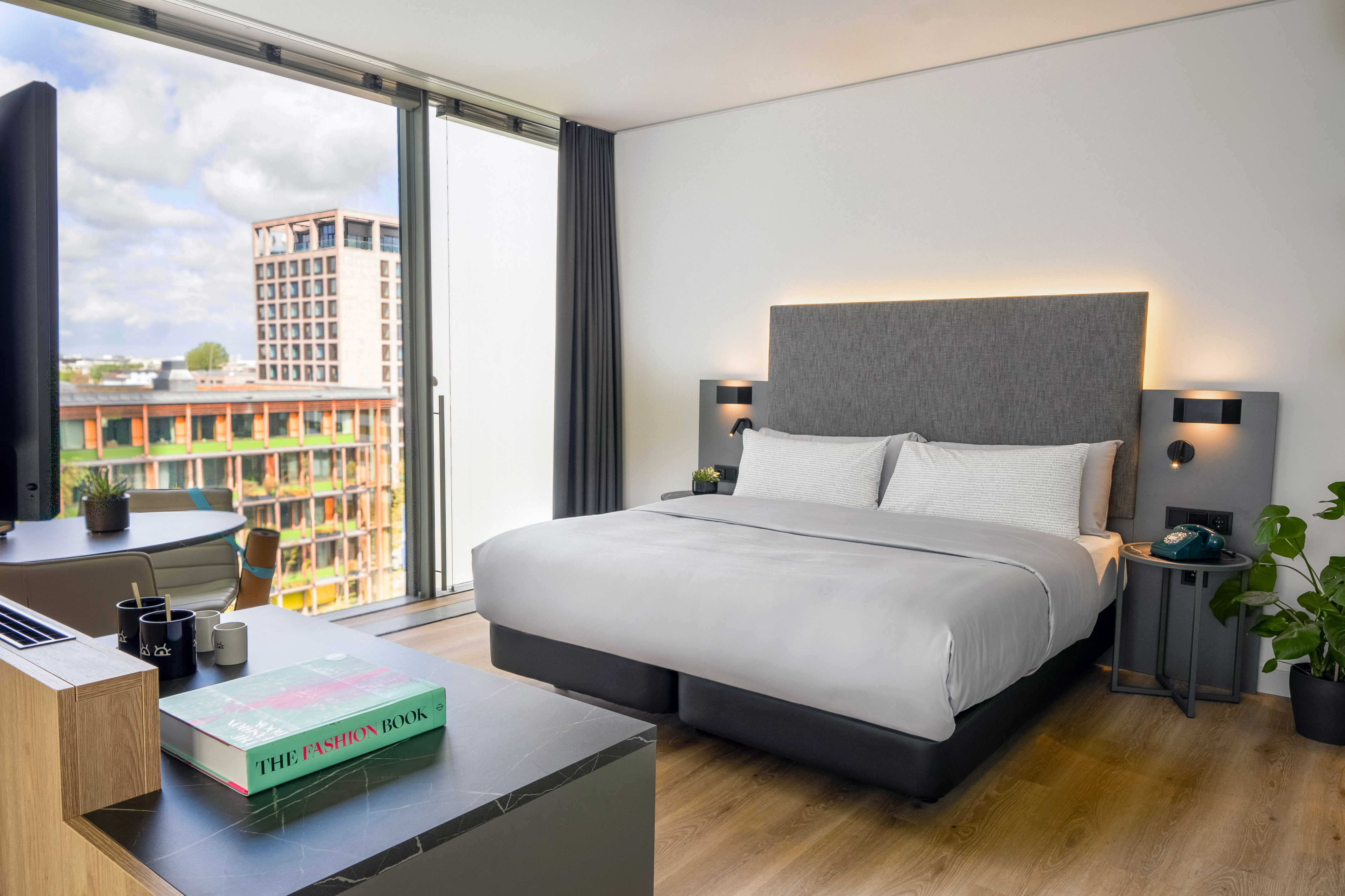 Modern hotel bedroom with city view, comfortable bed, and desk.