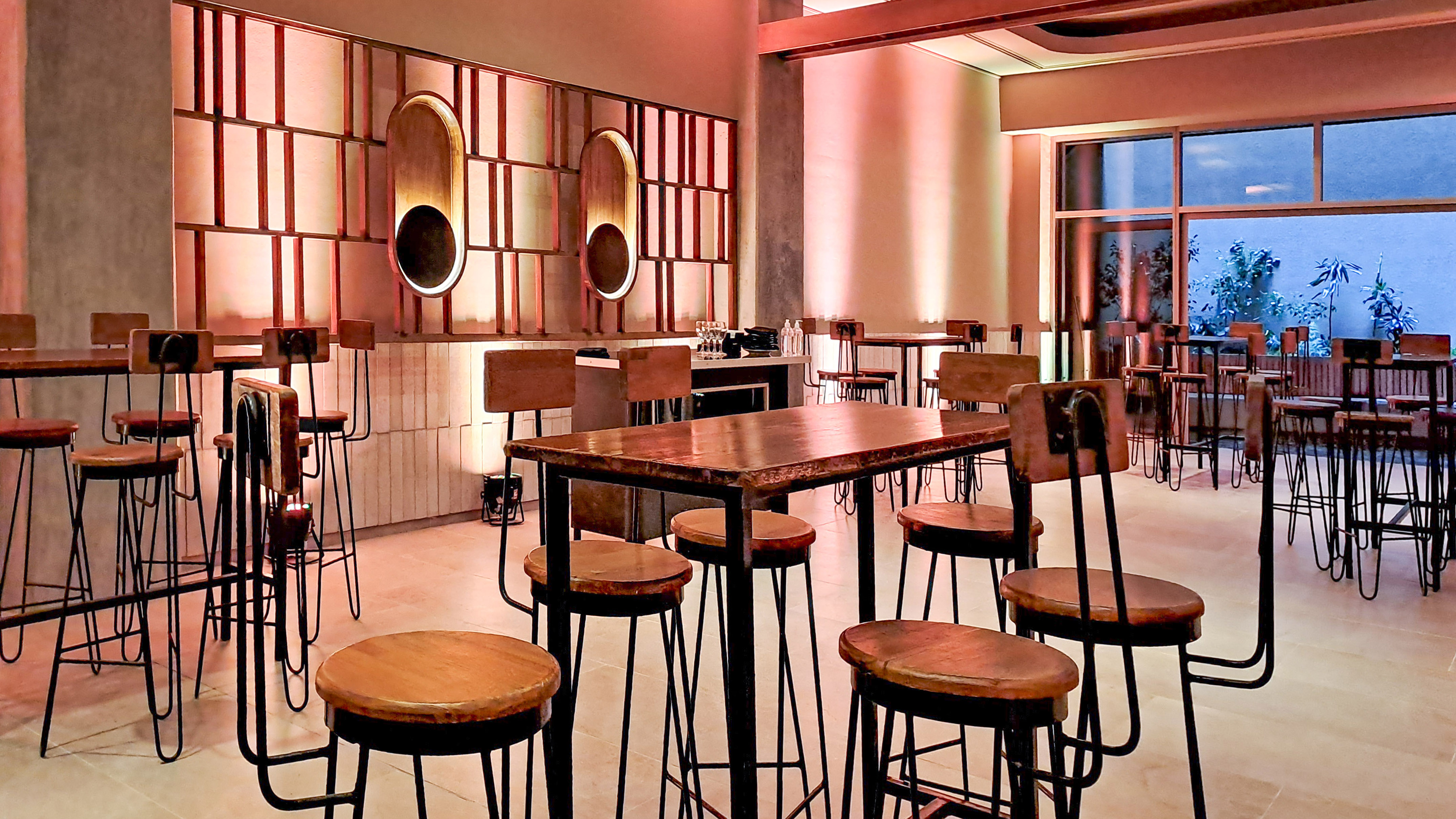 Modern bar interior with wooden high tables, stools, and warm ambient lighting.