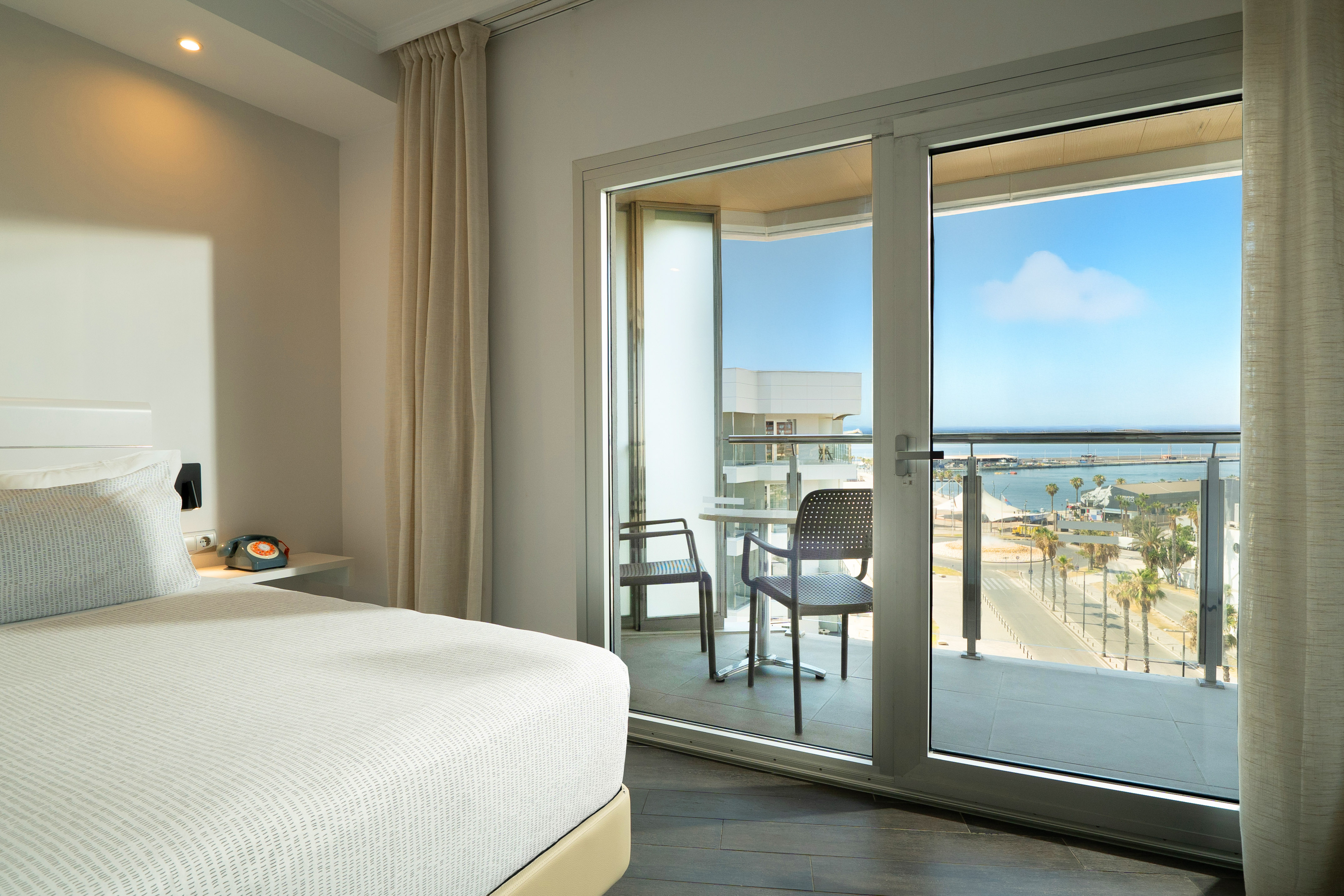 Modern hotel room with bed, private balcony, and harbor sea view.