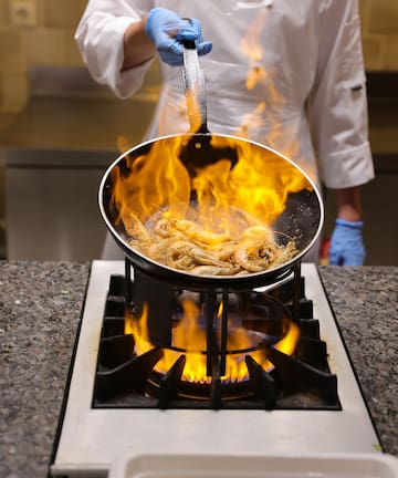 a chef cooking food on a pan over a fire