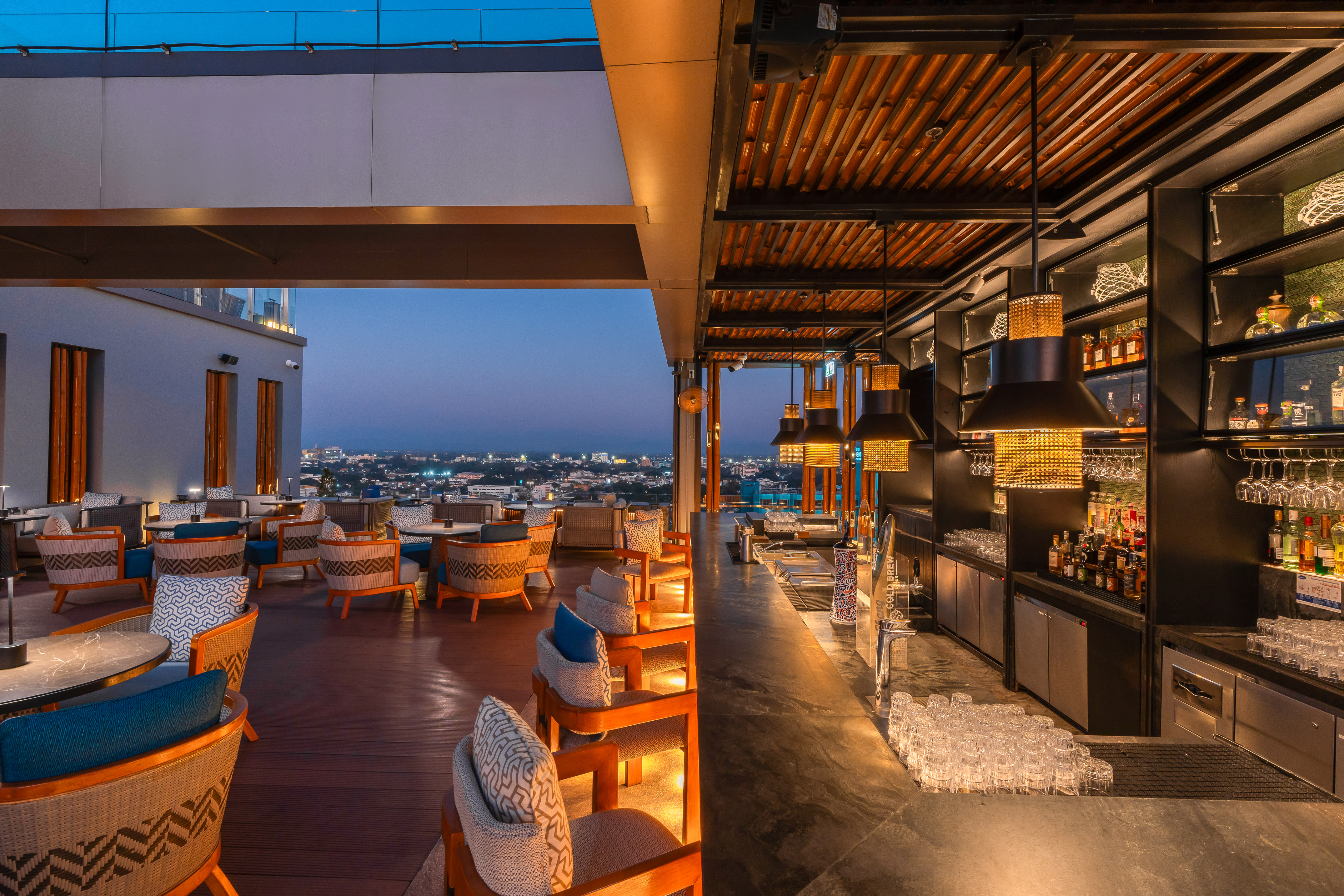 Evening rooftop bar with stylish lounge, illuminated bar, and city views.