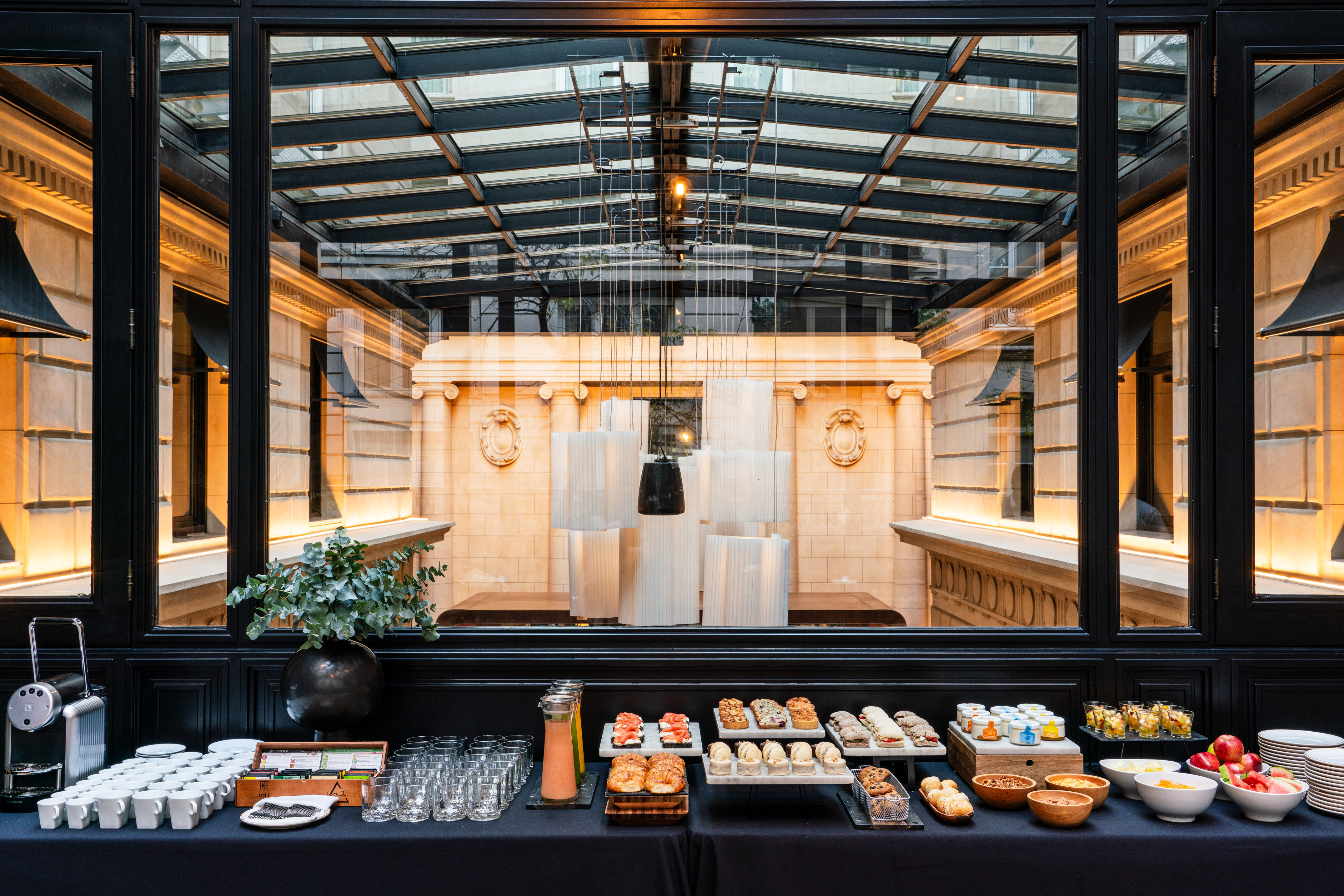 Gourmet breakfast buffet, pastries, fresh fruit, coffee, elegant glass enclosure.