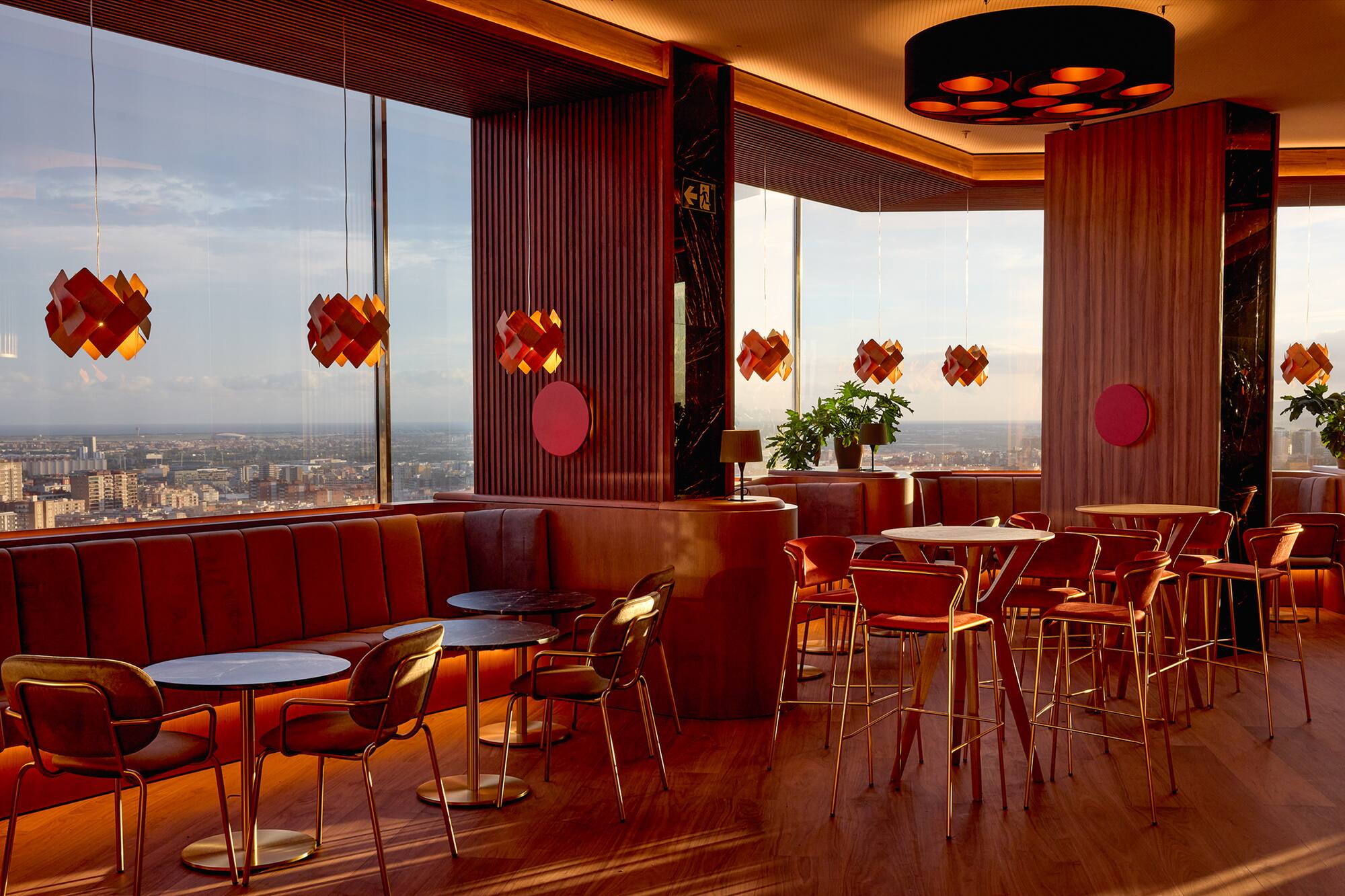Stylish bar interior with panoramic city view and warm red furnishings.