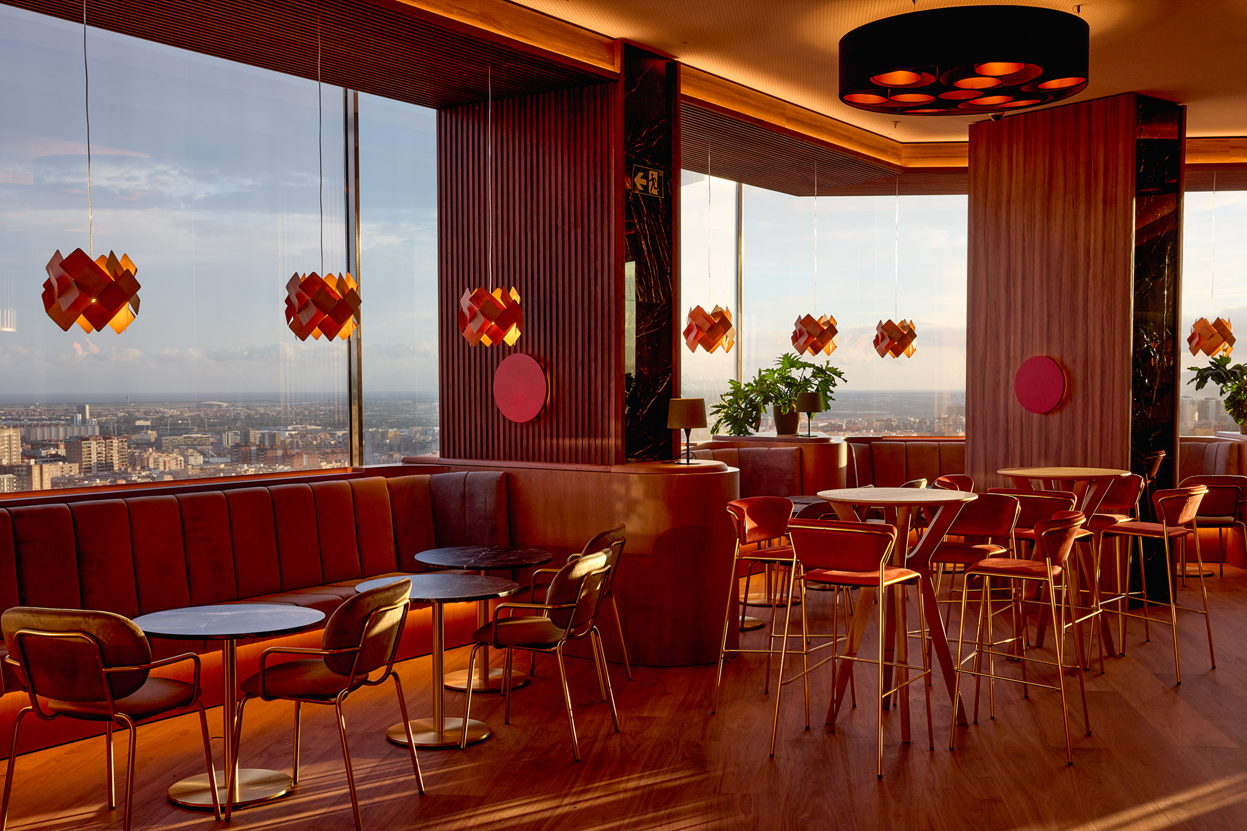 Stylish bar interior with panoramic city view and warm red furnishings.