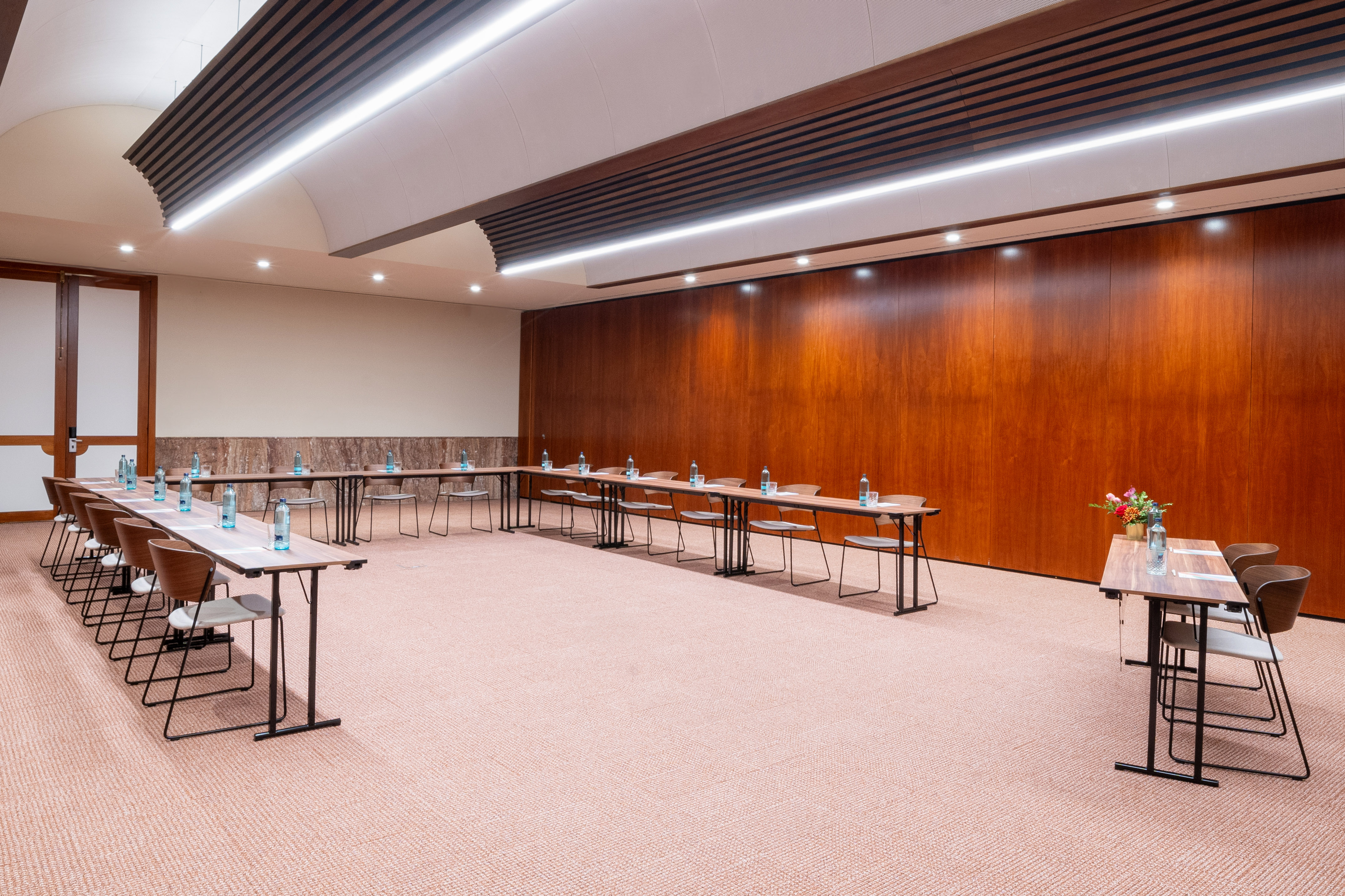 Modern U-shaped meeting room with wood walls, linear lighting, and tables.